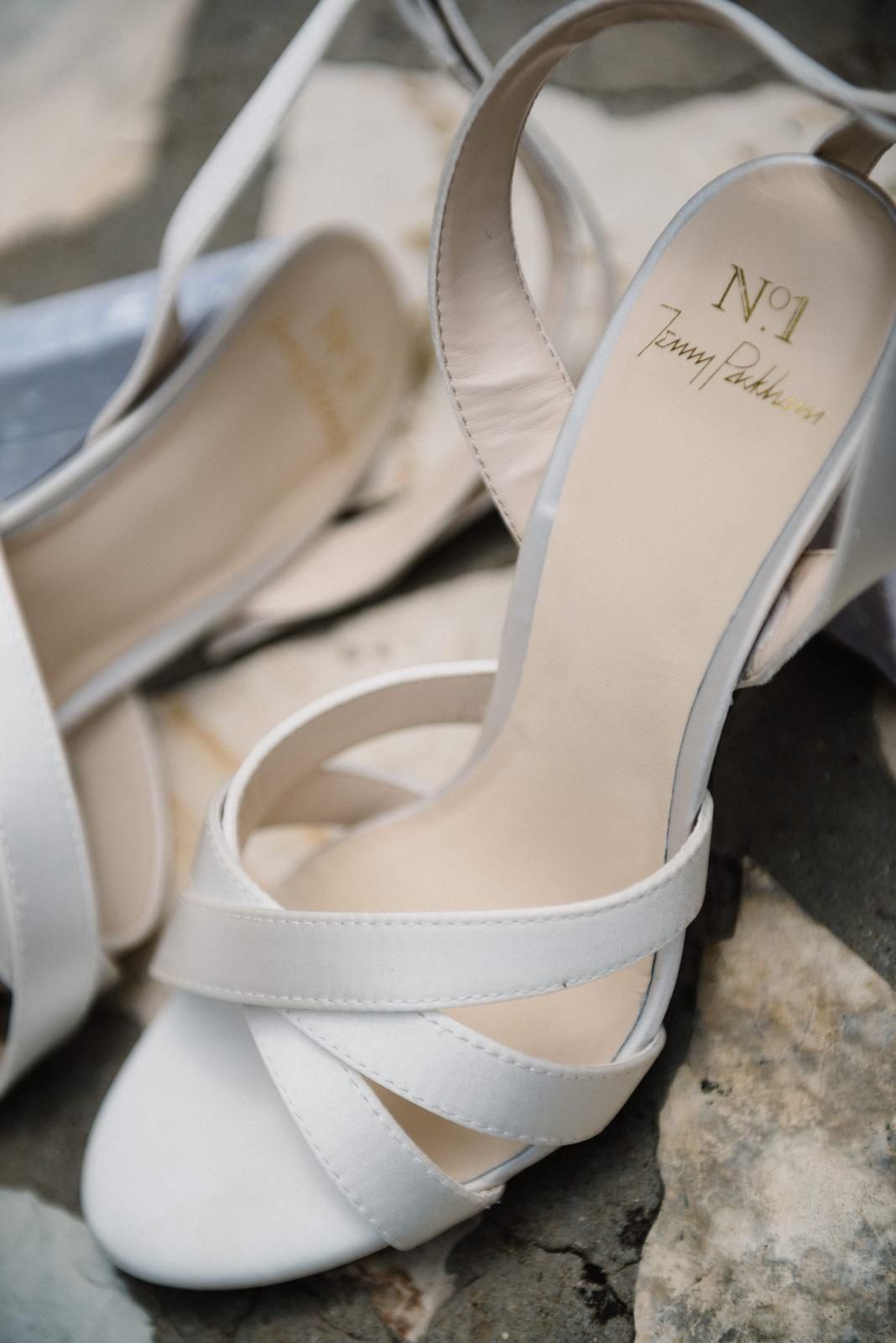 Elegant white bridal heels with crossed straps photographed on stone surface.