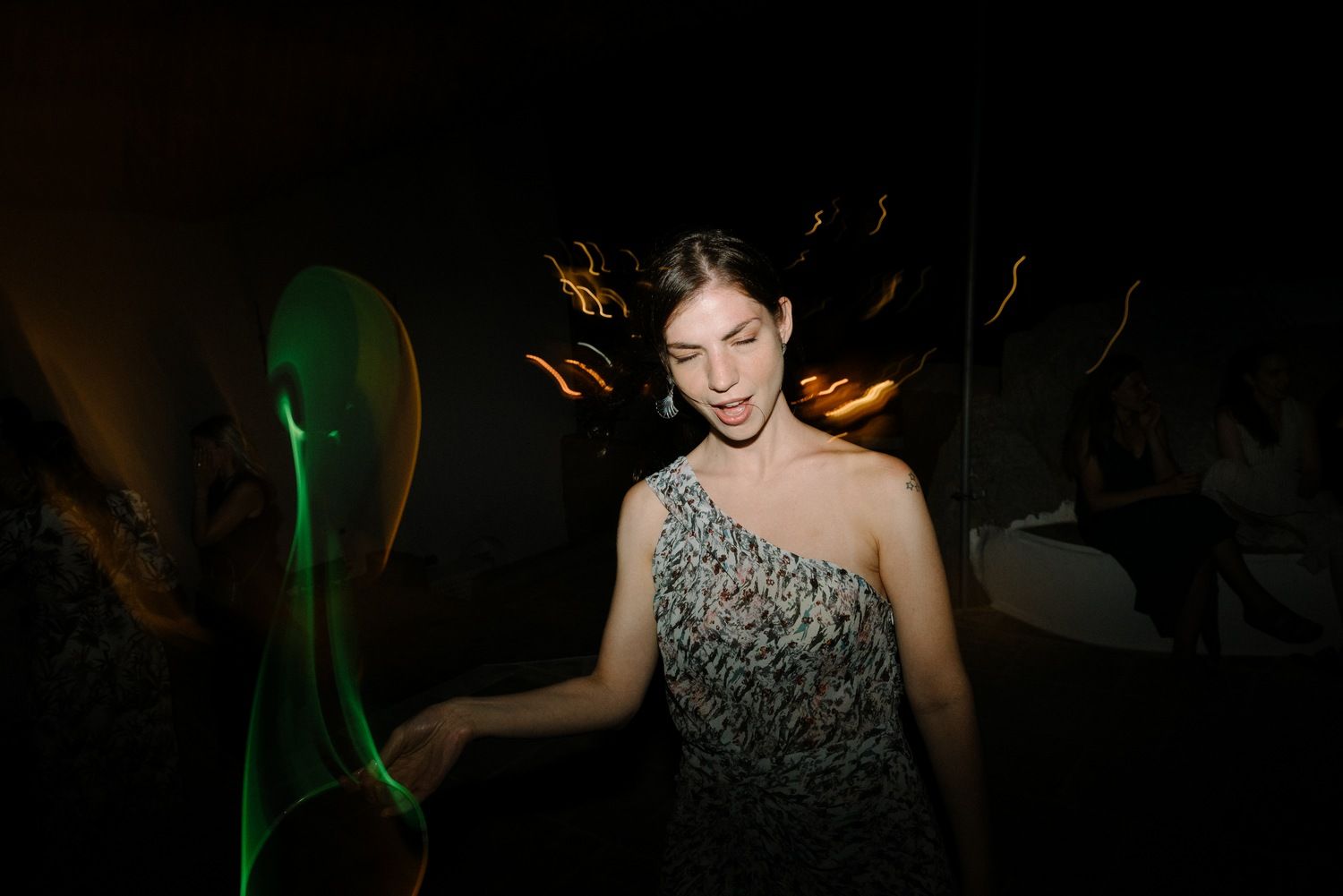 Woman in sparkly dress dances at party with green light effects in background.