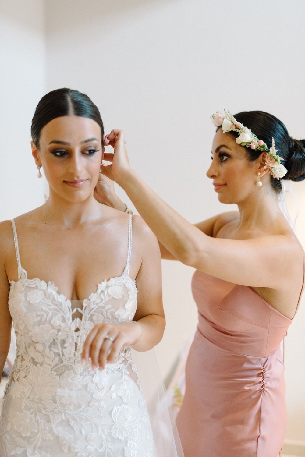 Bridesmaids in blush pink dresses helping adjust wedding day accessories and jewelry.