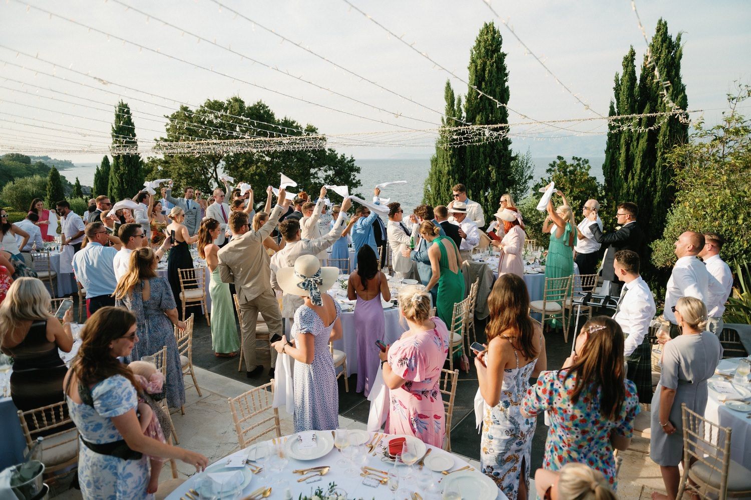 Large crowd of wedding guests celebrating outdoors with drinks and dancing.