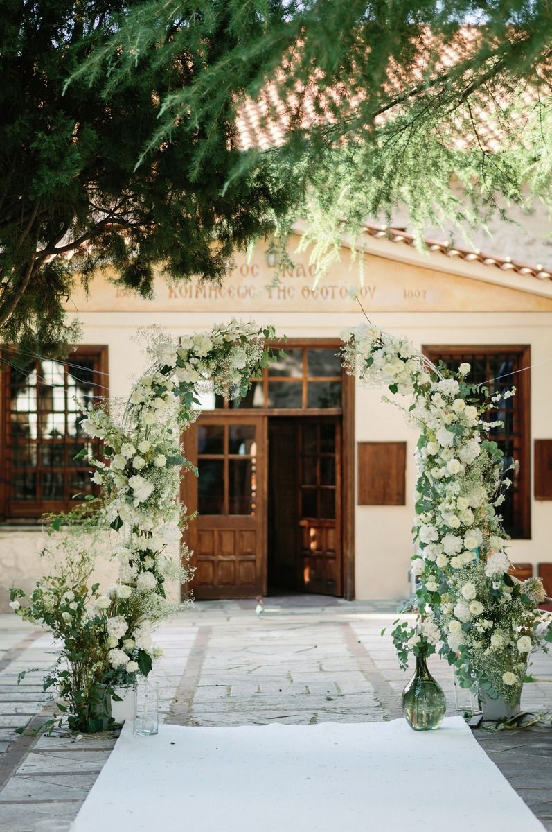 Beautiful floral arch with white roses frames entrance to venue for outdoor wedding ceremony.