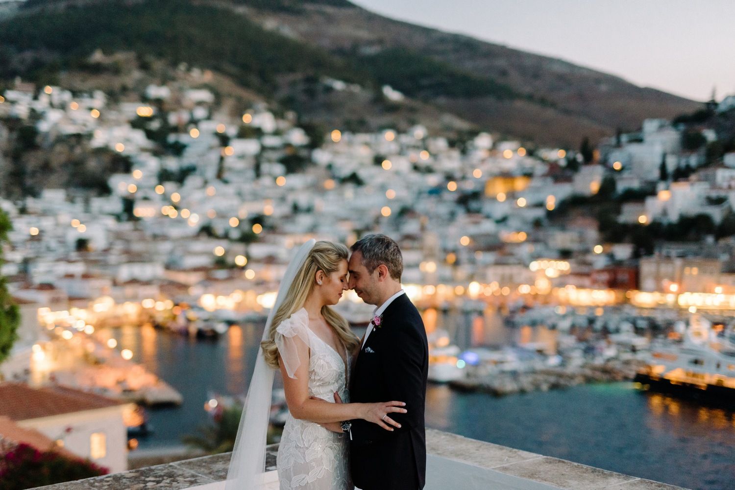 Romantic wedding portrait against hillside Mediterranean town with harbor lights.
