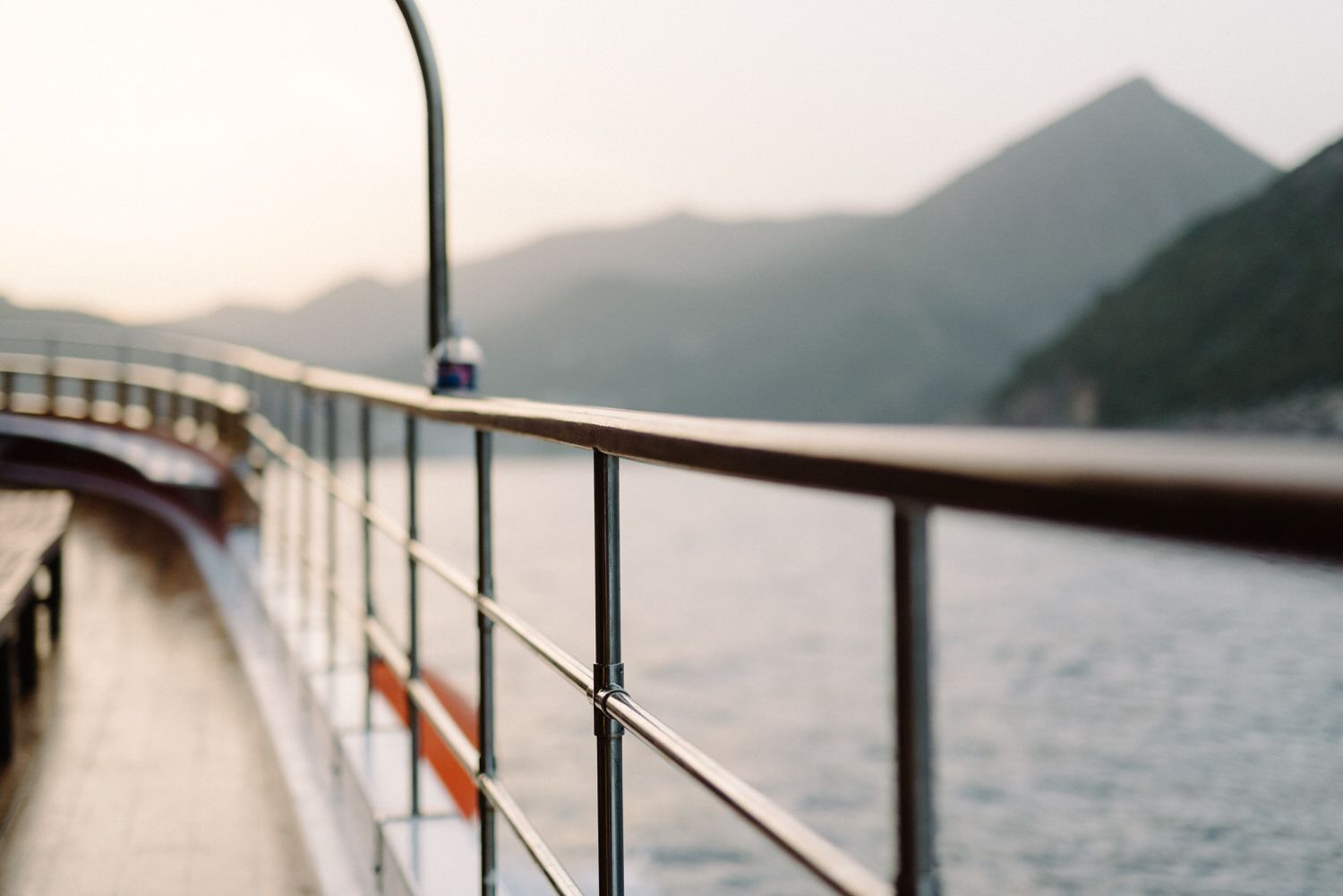 Scenic view of curving ship railing with mountains and sea at sunset.