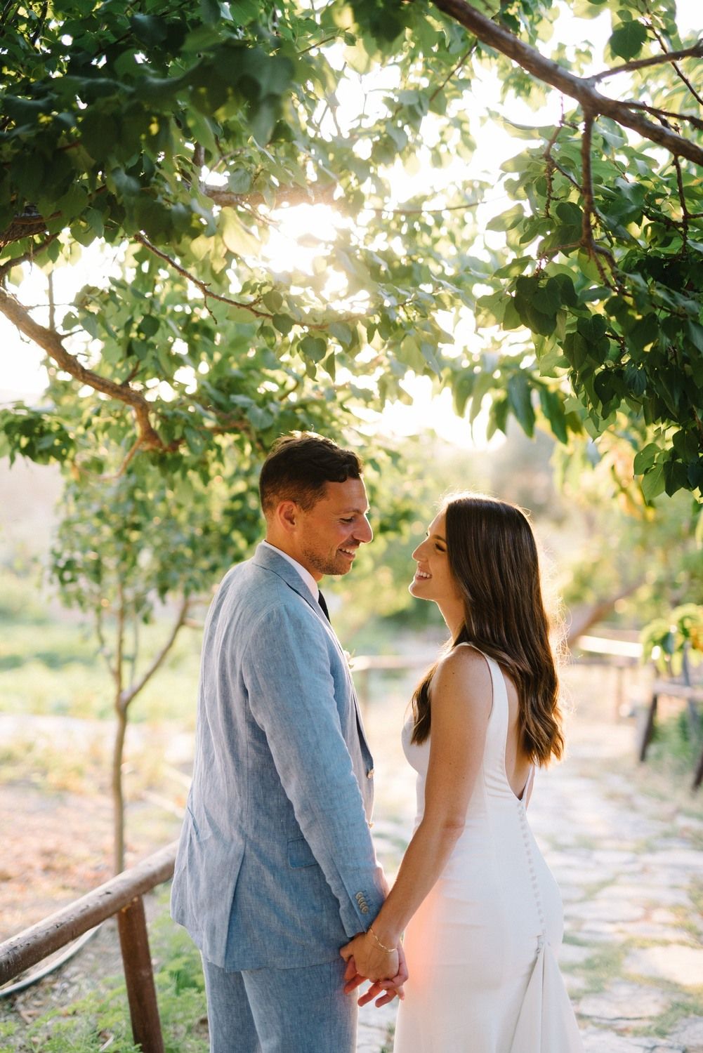 Newlyweds hold hands while sharing an intimate moment in a garden setting with dappled sunlight.
