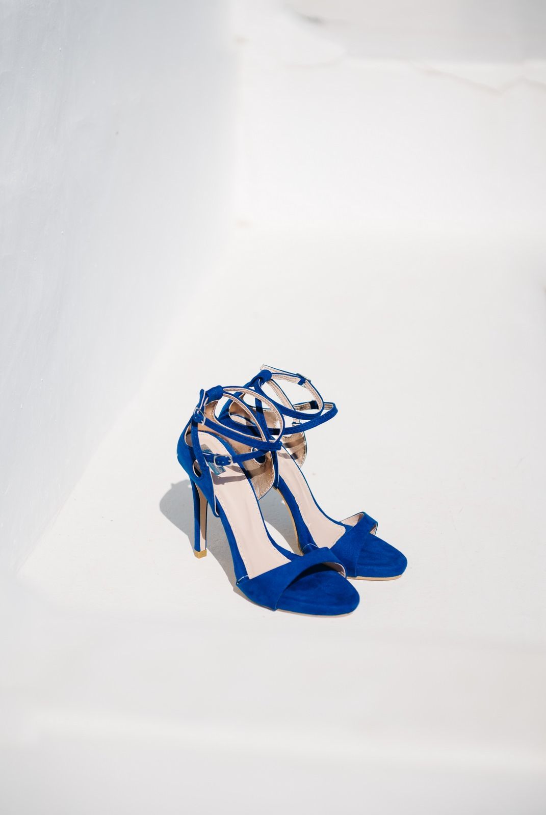 Bright blue suede high heel sandals with ankle straps against white background.