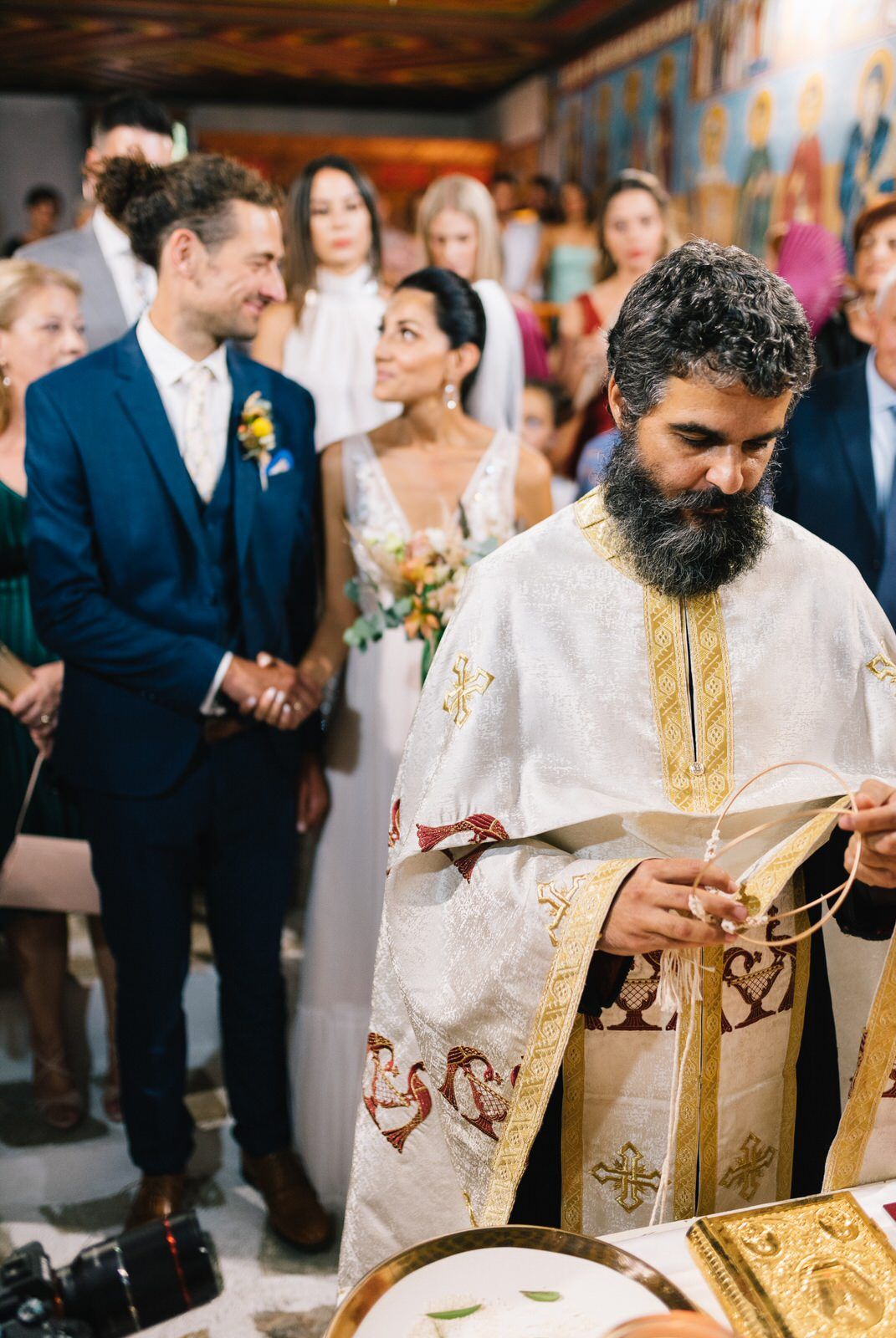 Orthodox priest conducts wedding ceremony in decorated church with colorful murals.