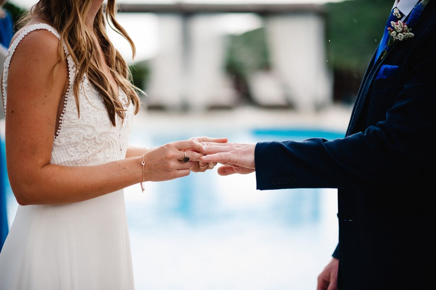 Exchange of rings during outdoor wedding ceremony with pool in background.
