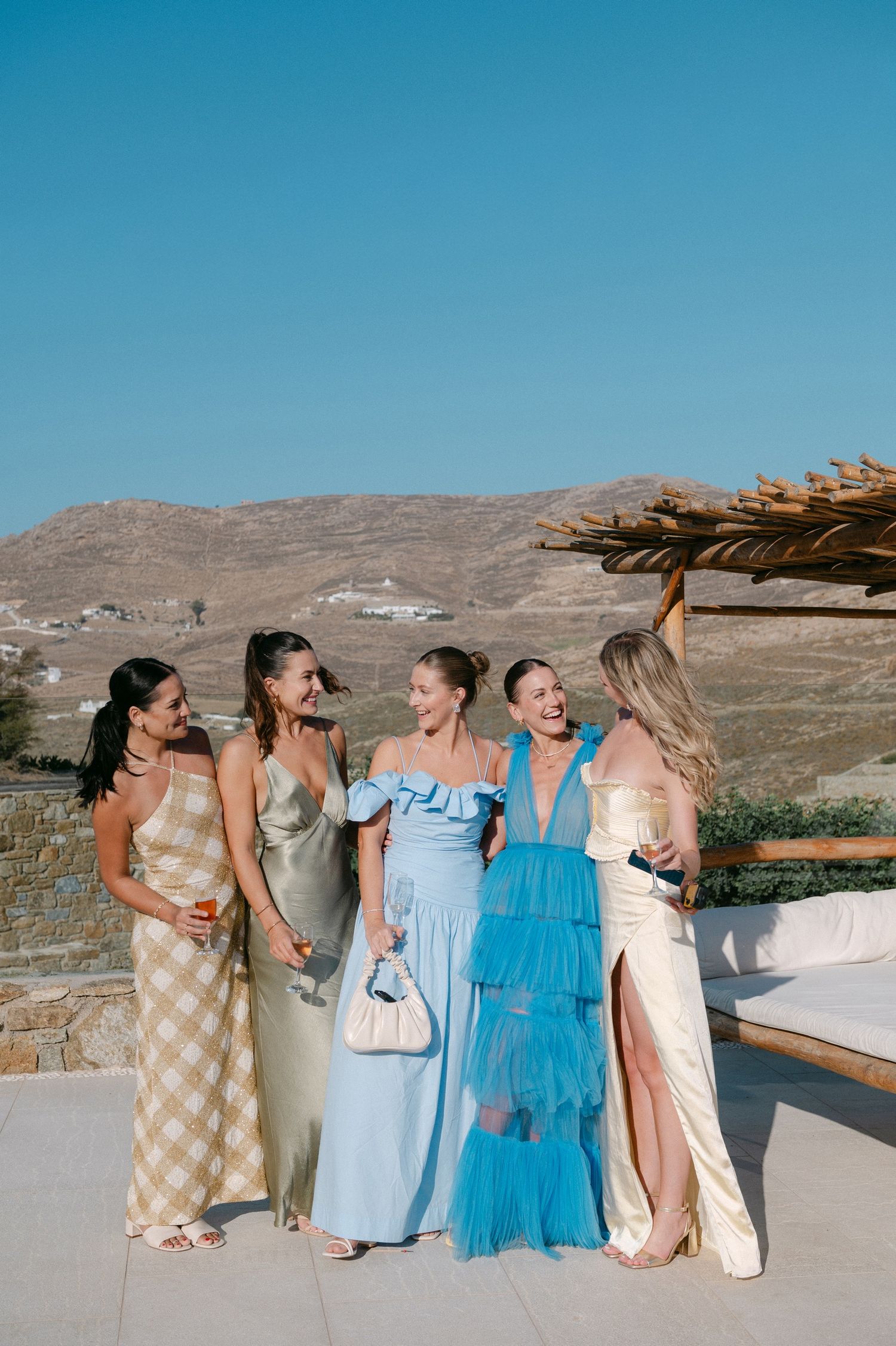 A group in coordinated dresses laugh and smile together against a desert mountain backdrop.