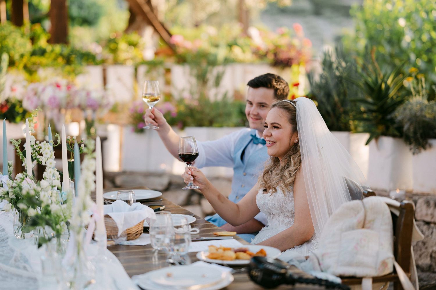 A couple celebrates at an elegant outdoor dinner table decorated with candles and flowers during sunset.