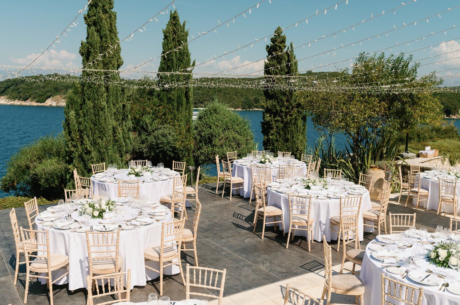 Elegant outdoor wedding reception setup with string lights and ocean view.