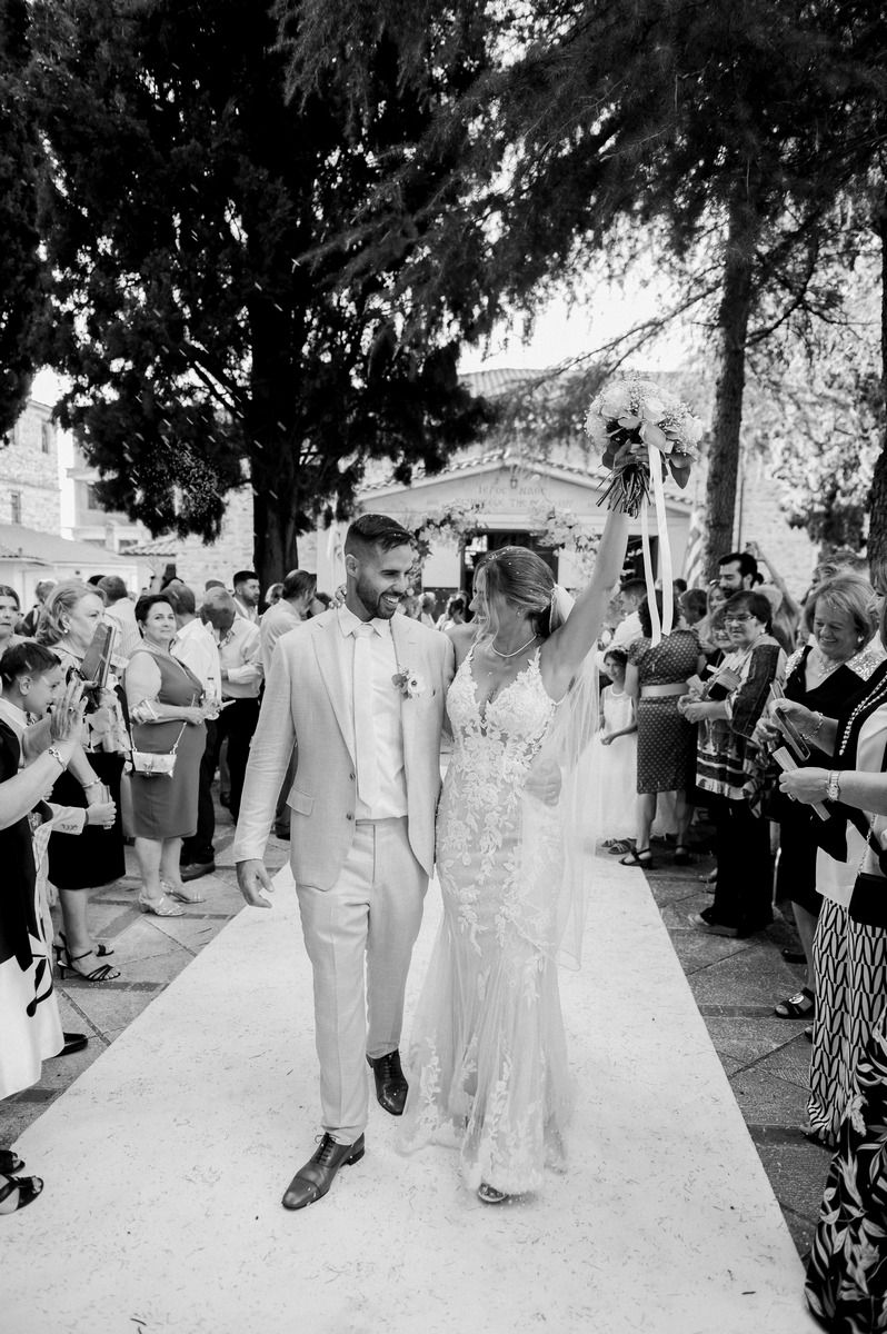 Wedding couple walks down outdoor aisle as guests celebrate in black and white photography.
