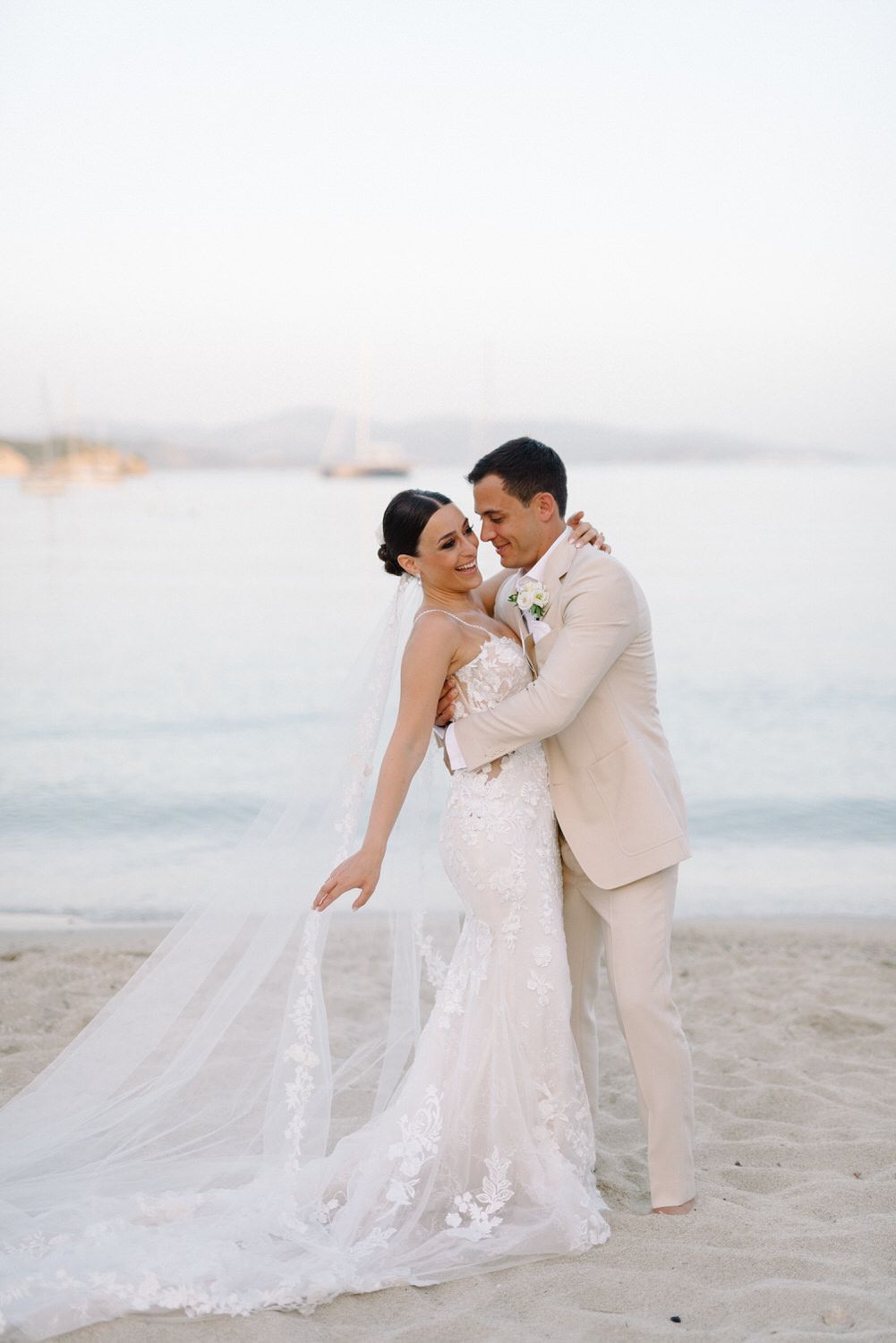 A romantic beach wedding portrait with a couple in light-colored attire and flowing veil.