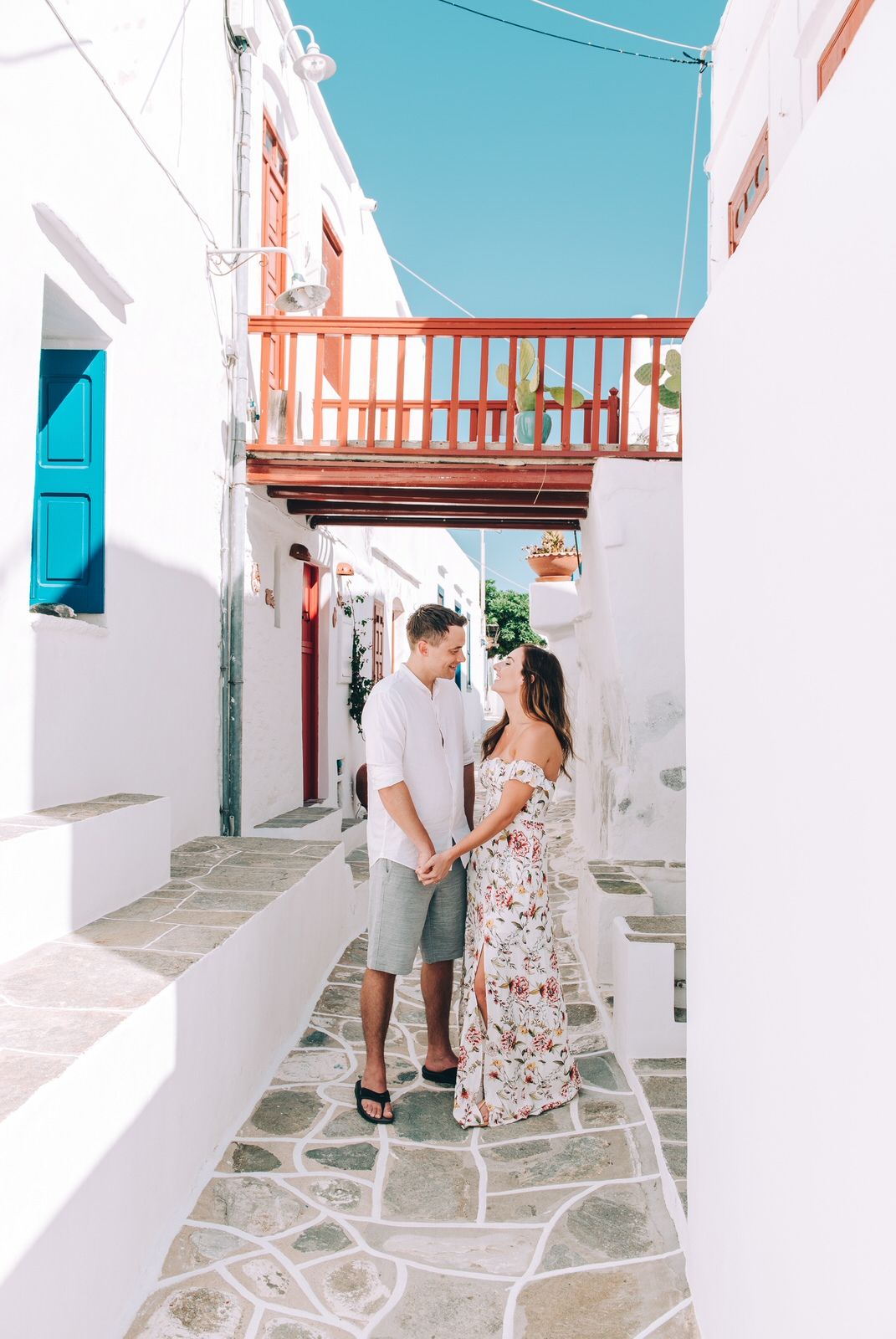 A romantic scene in a narrow whitewashed Greek alley with blue doors and wooden balcony.