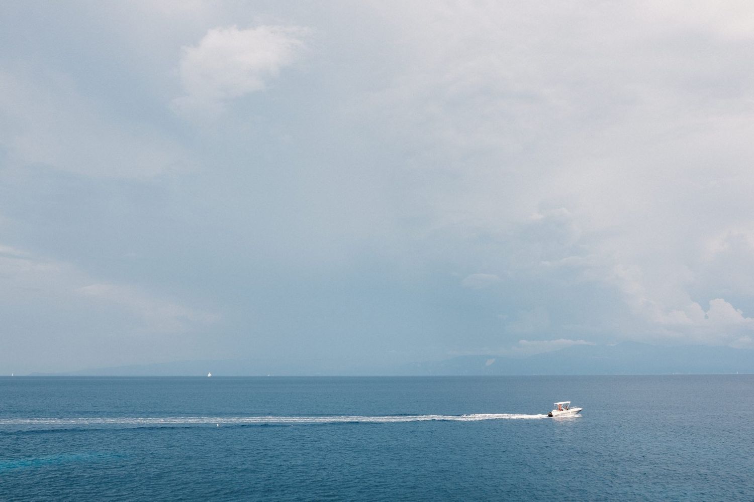Serene seascape with a small boat creating a white wake against blue ocean waters.