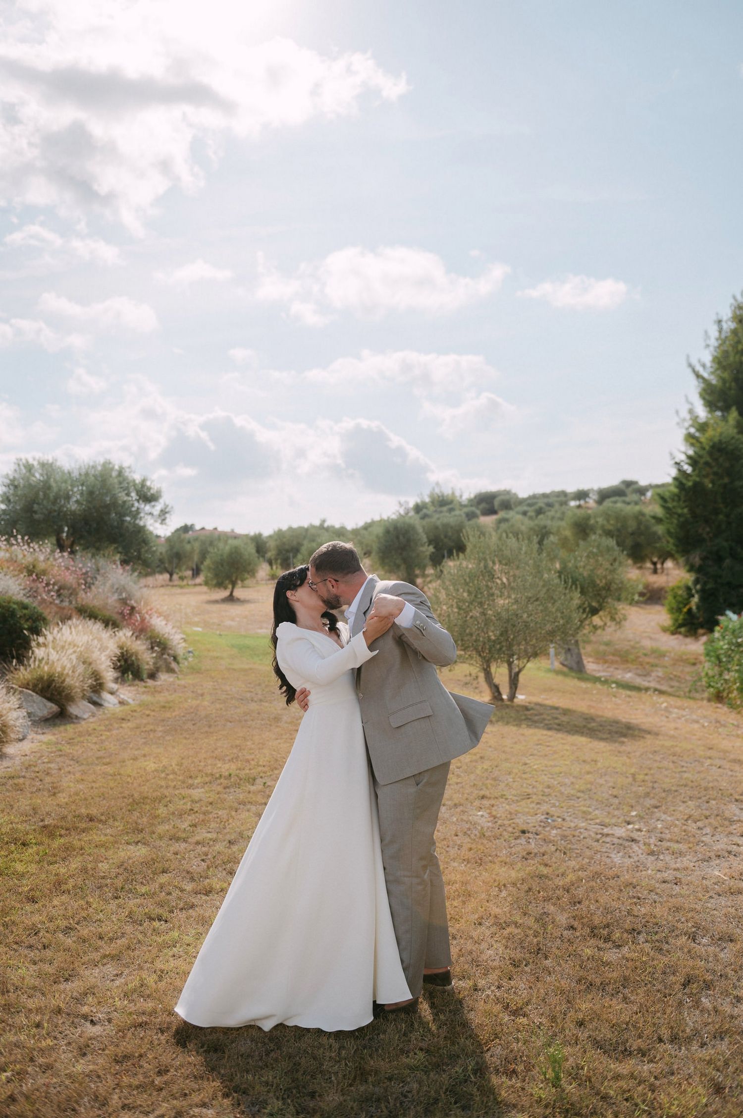 A couple in wedding attire share romantic moments in an olive grove with a dreamy, natural backdrop.