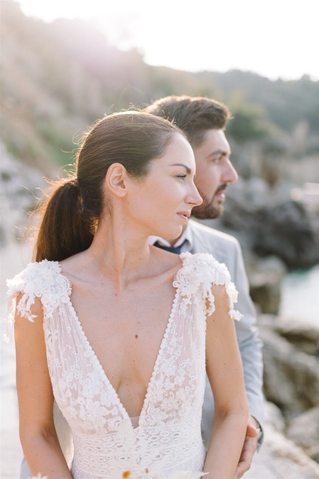 A couple in wedding attire pose together outdoors during golden hour, with soft sunlight creating a romantic atmosphere.
