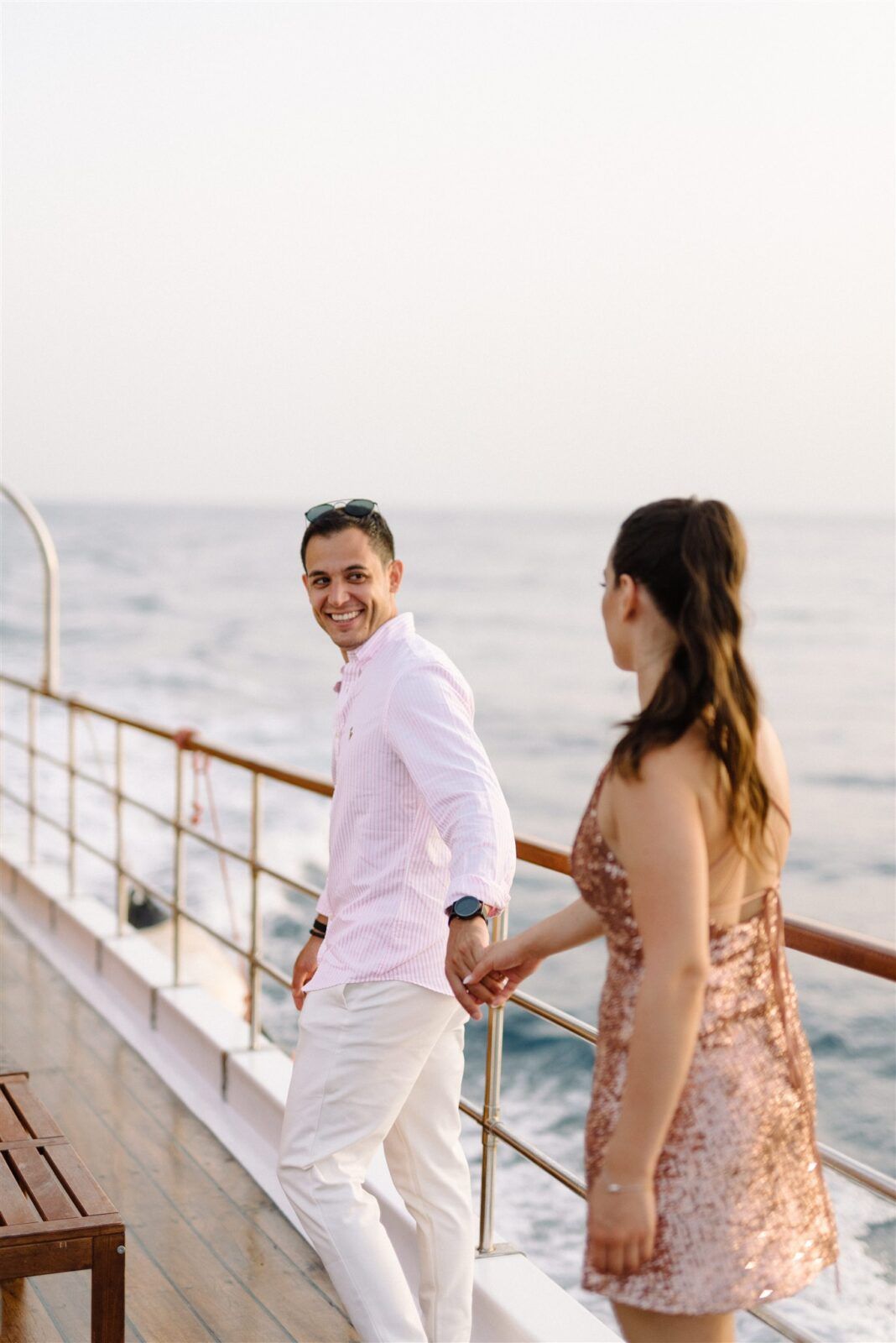 A couple enjoys a romantic moment on a cruise ship deck at sunset, with the ocean visible in the background.