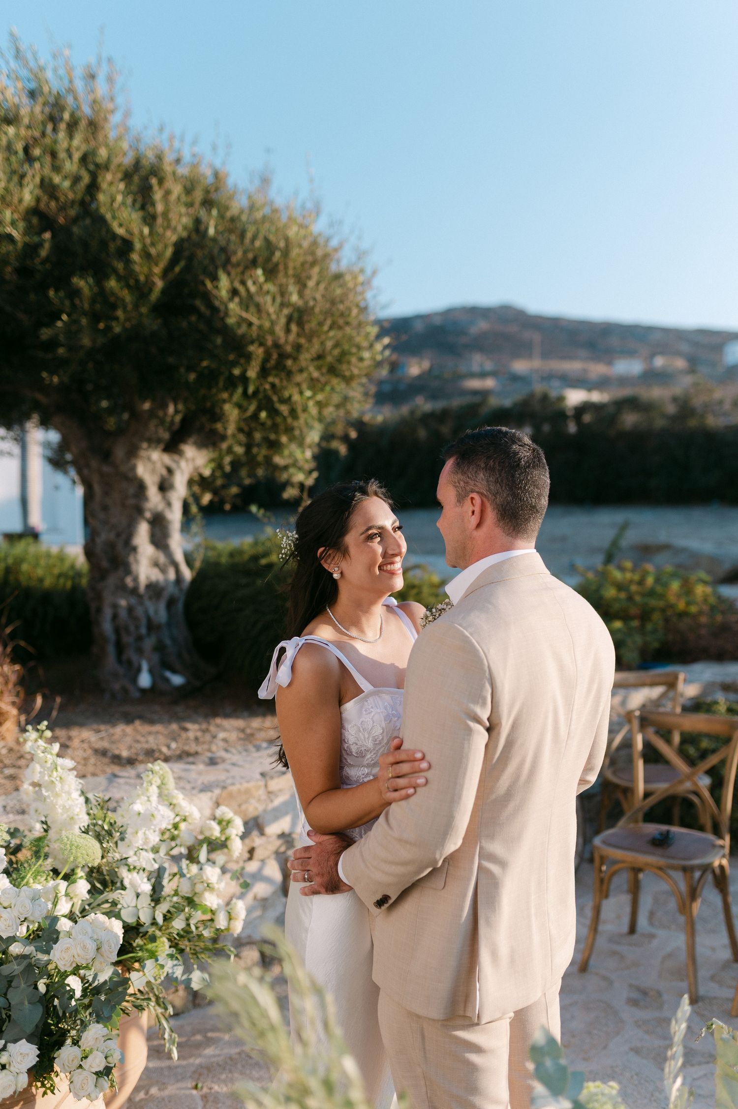 A couple shares a romantic dance moment at an outdoor wedding venue with mountains and floral arrangements in the background.