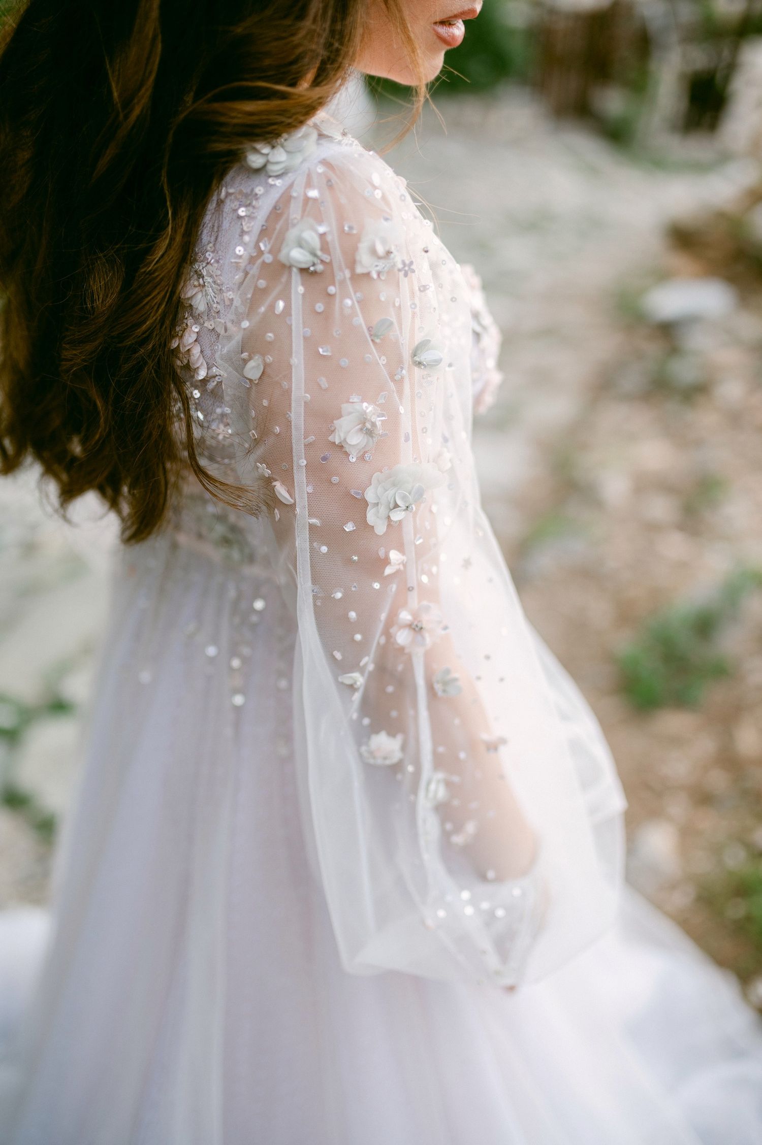 Ethereal sheer wedding dress sleeve with delicate floral lace appliques and tulle details captured in soft natural light.
