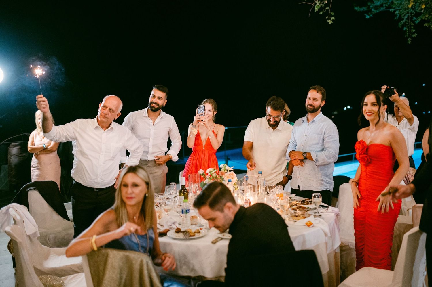 Dinner party guests enjoying an outdoor evening celebration with white tablecloths and festive atmosphere.