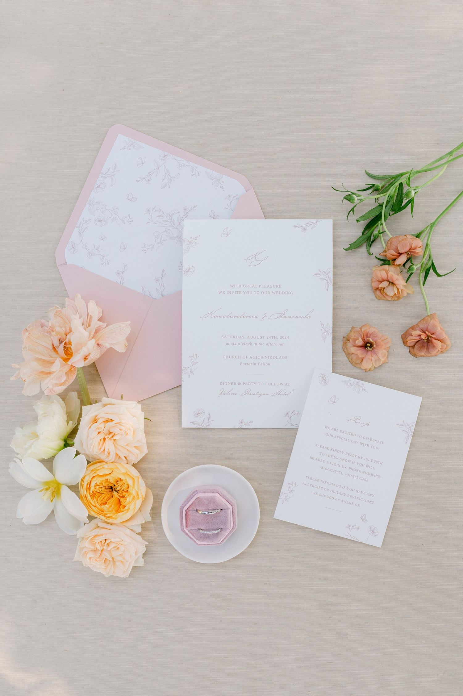 Wedding invitation suite with peach and white flowers, pink envelope, and ring dish on light beige background.