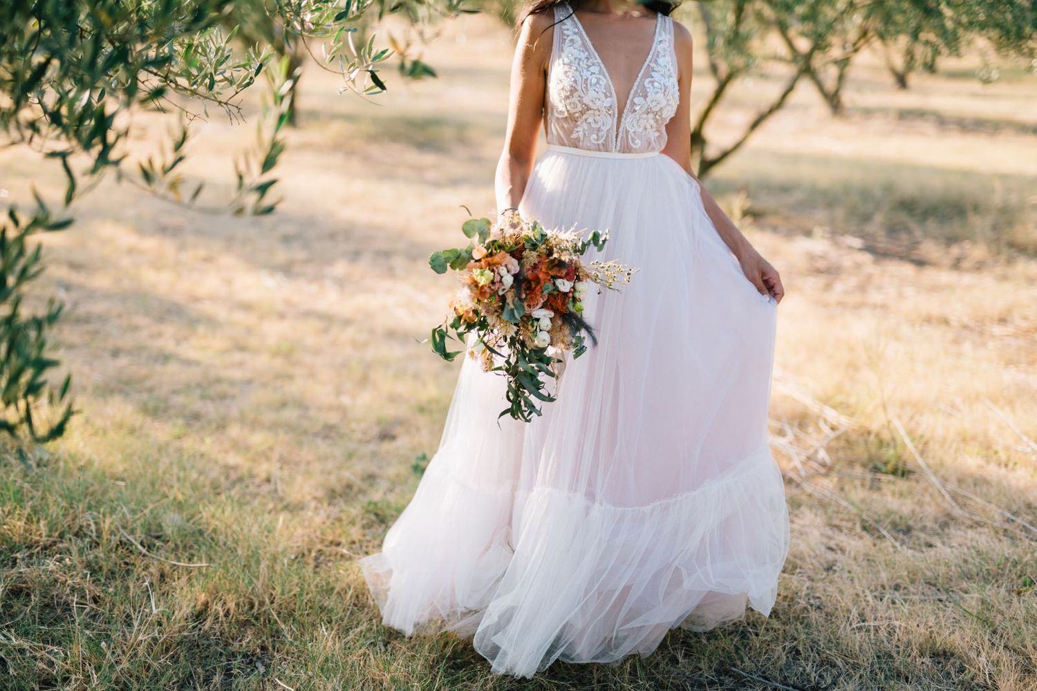Close-up of flowing white wedding dress with delicate lace details and autumn-toned bouquet.