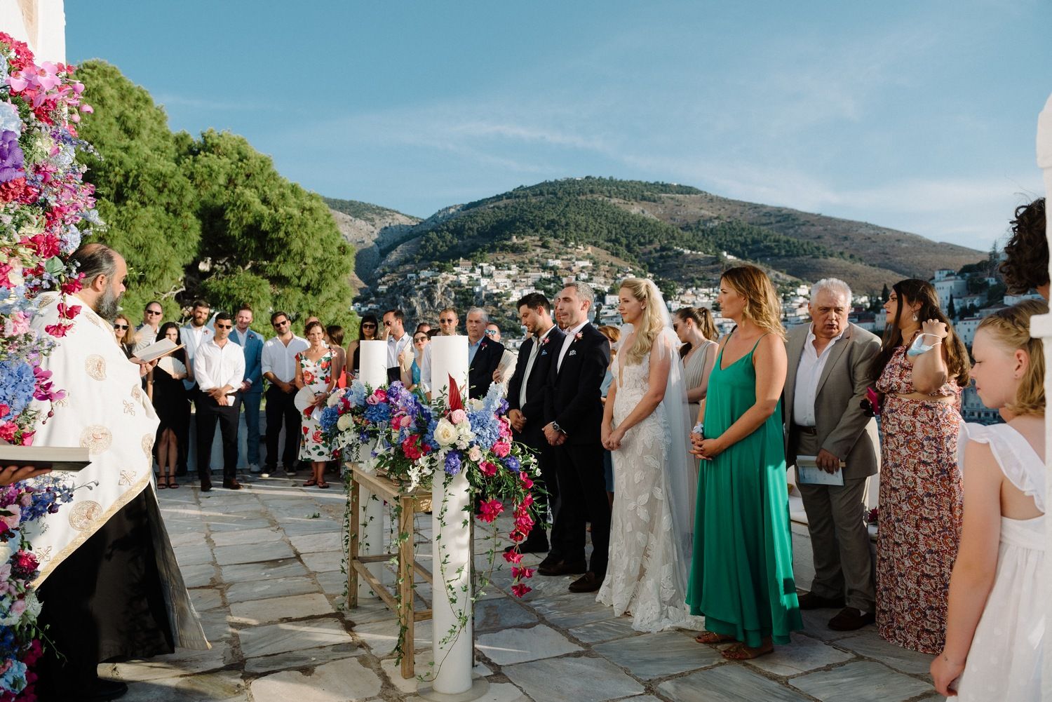 Wedding guests gathered on a stone terrace with vibrant floral arrangements and mountain views in the background.