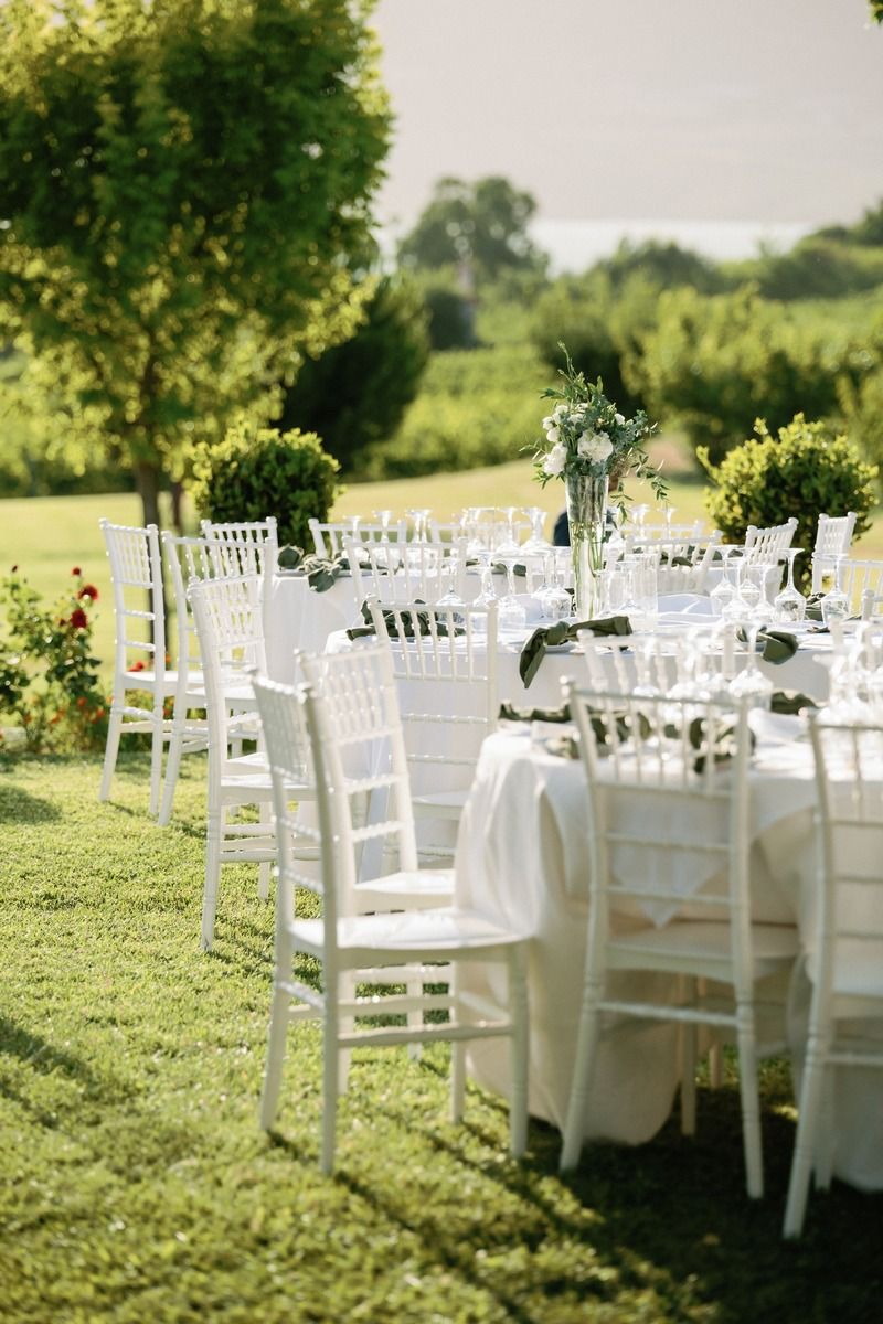 White Chiavari chairs and elegant table settings arranged on manicured lawn for outdoor reception.