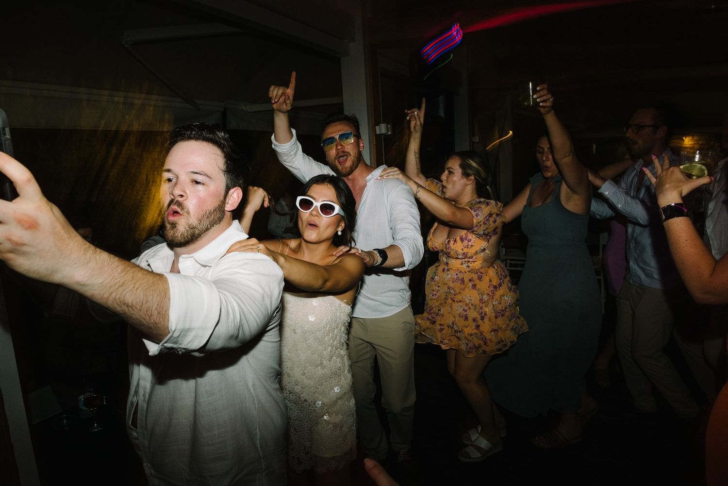 Guests dance and raise their hands in celebration at a wedding reception party.