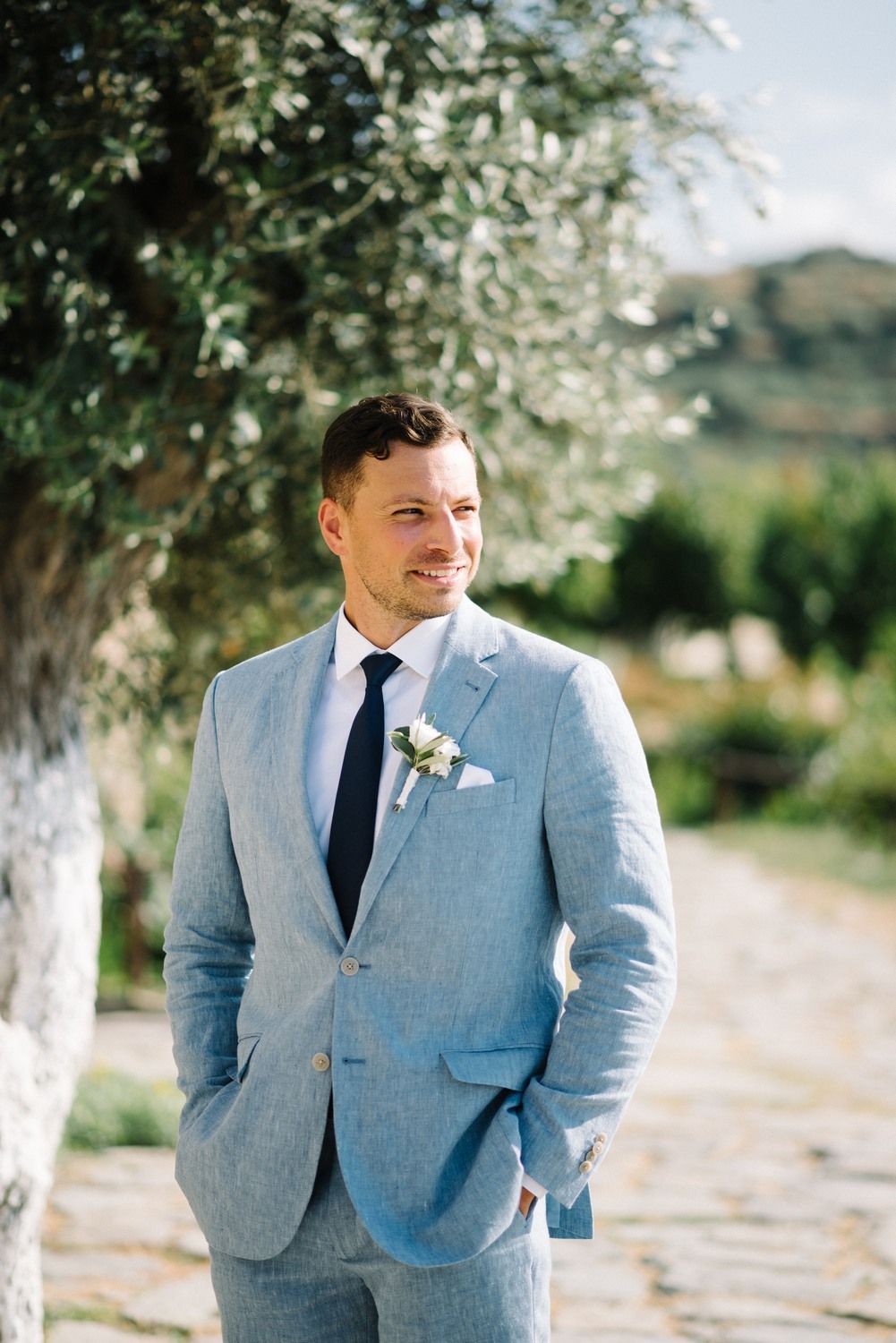 Portrait of groom in light blue suit with boutonniere against blurred garden background.