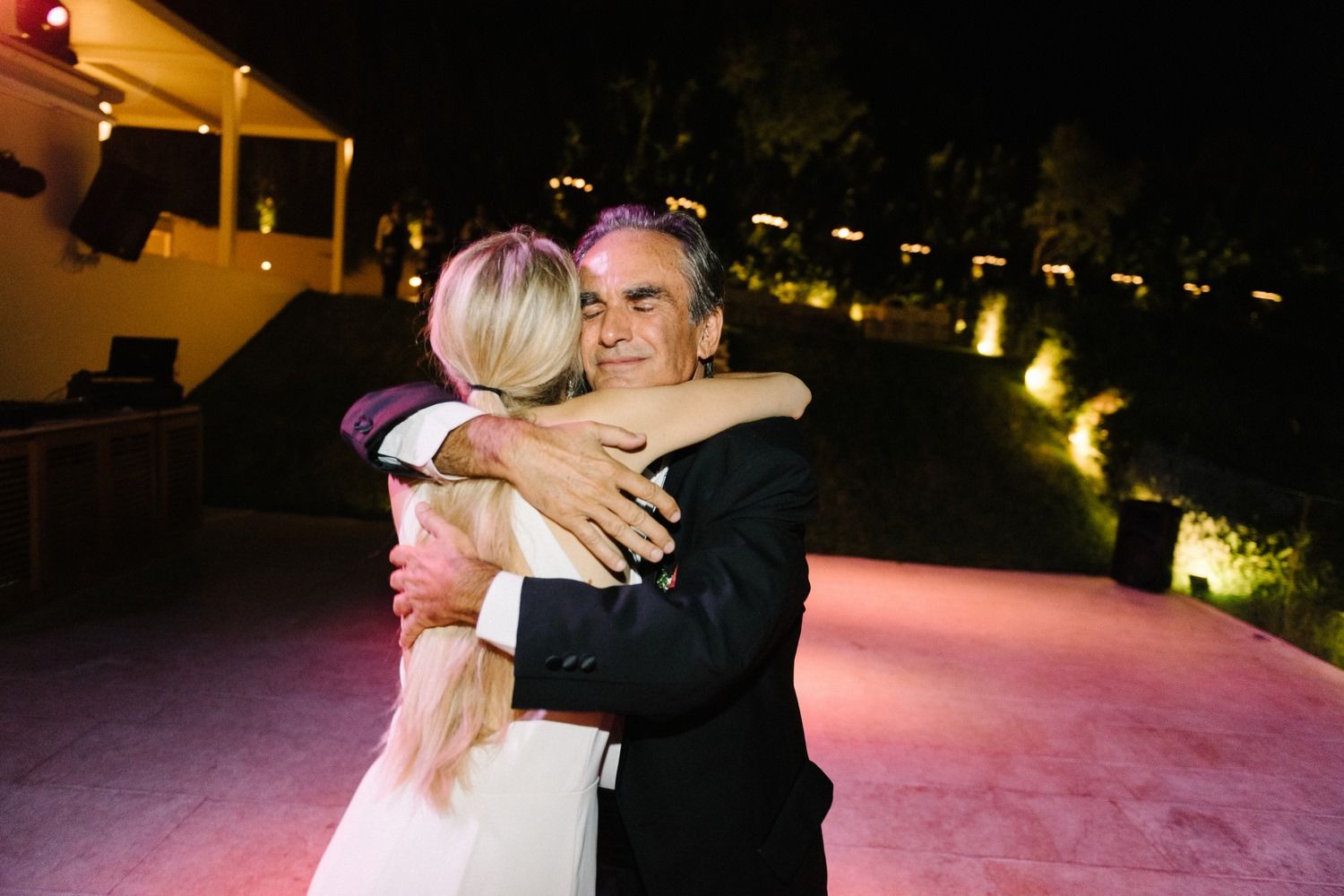 An emotional embrace on a lit dance floor during an evening celebration.