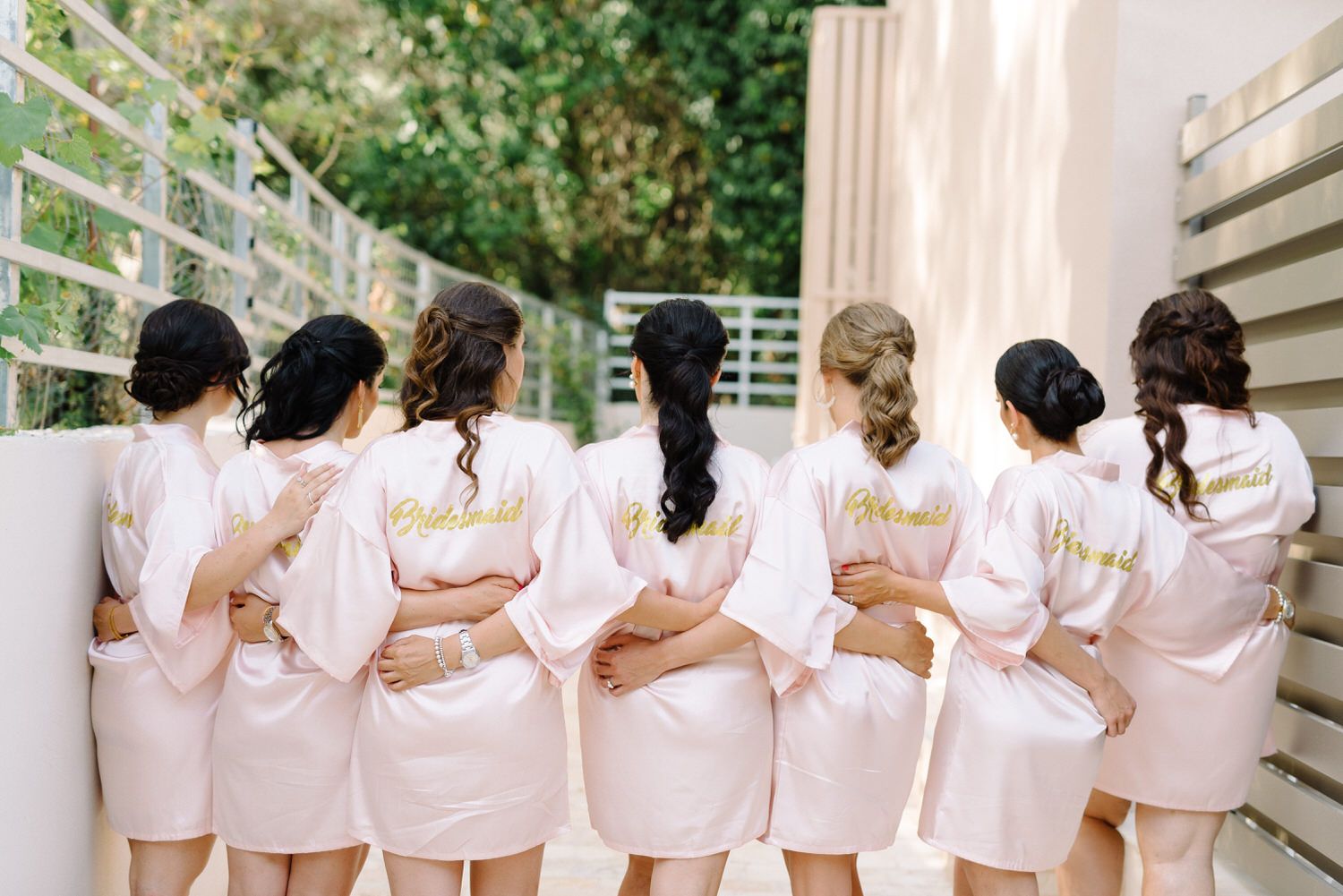 Bridesmaids in pink robes show off their matching outfits from behind.