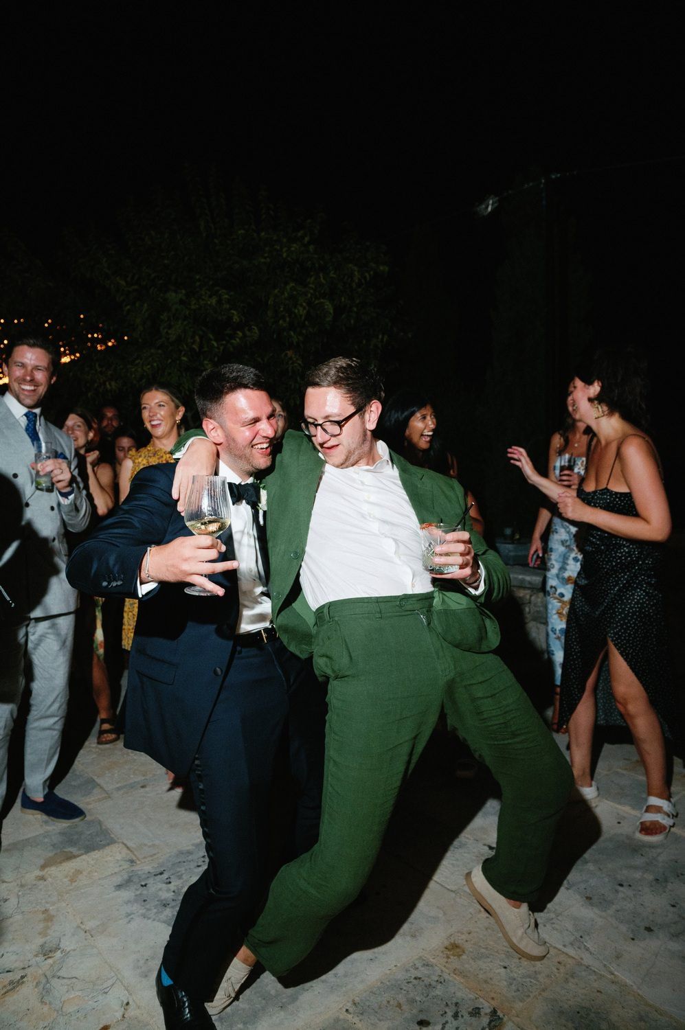 Friends in contrasting suits dancing energetically at a nighttime outdoor party.