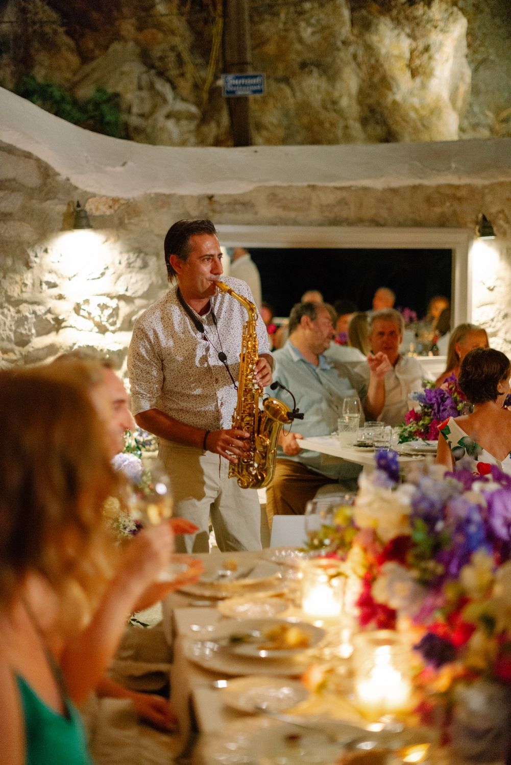 Musician playing saxophone during wedding reception dinner with candlelit tables.