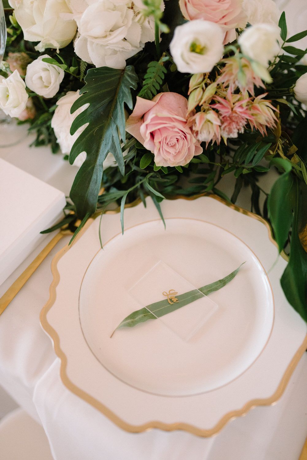 Close-up of luxurious table setting with pink and white roses, monstera leaves, and gold-rimmed plates.