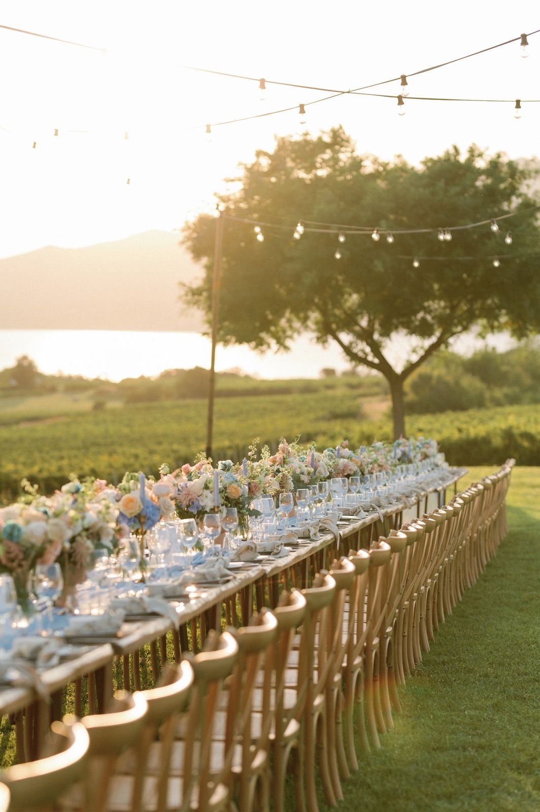 Long outdoor wedding reception table with string lights and sunset views across a scenic vineyard Kamkoutis in Velventos, Greece.