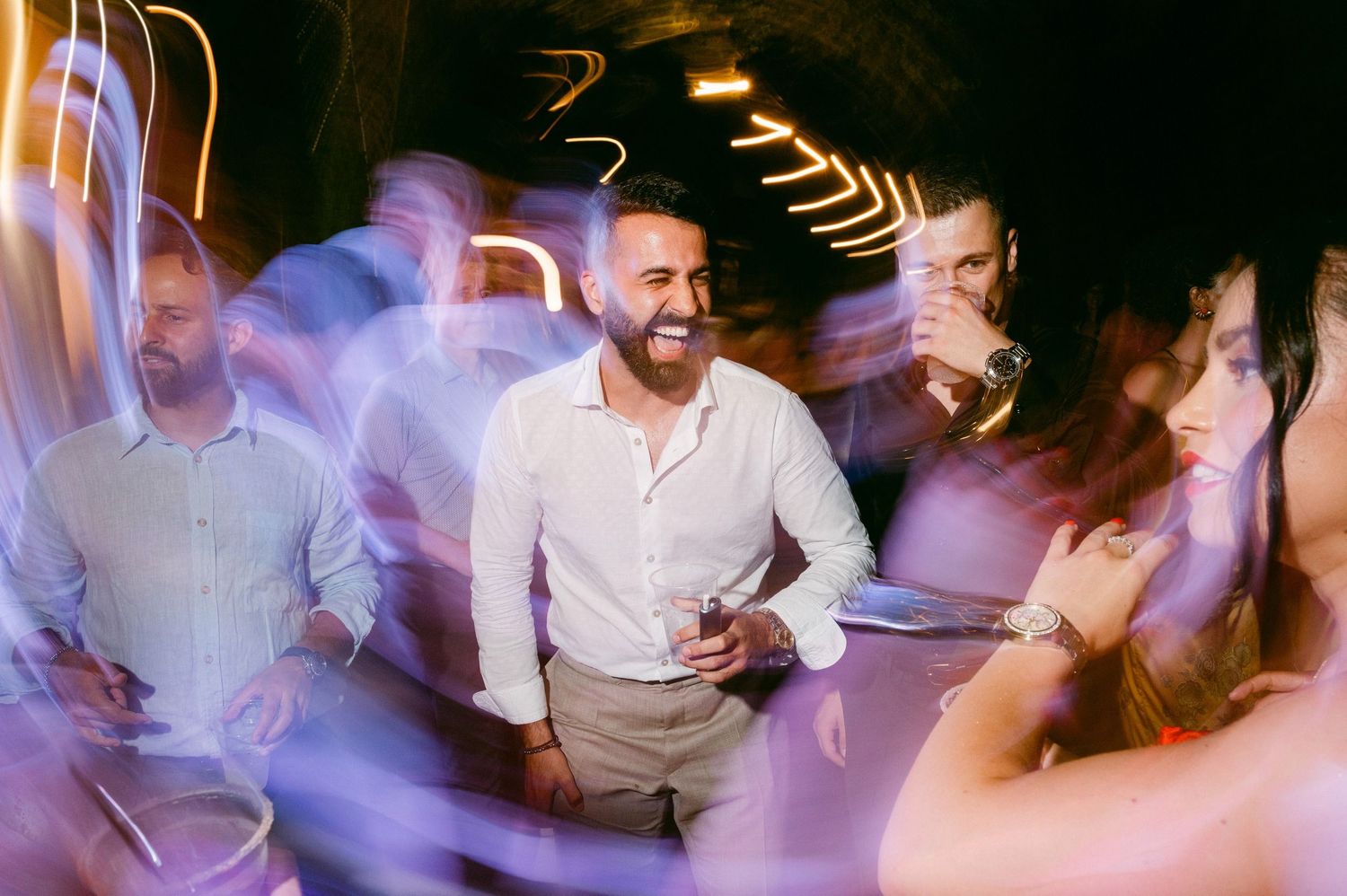 Party scene with guests dancing and moving on dance floor creating motion blur light trails in nighttime setting.