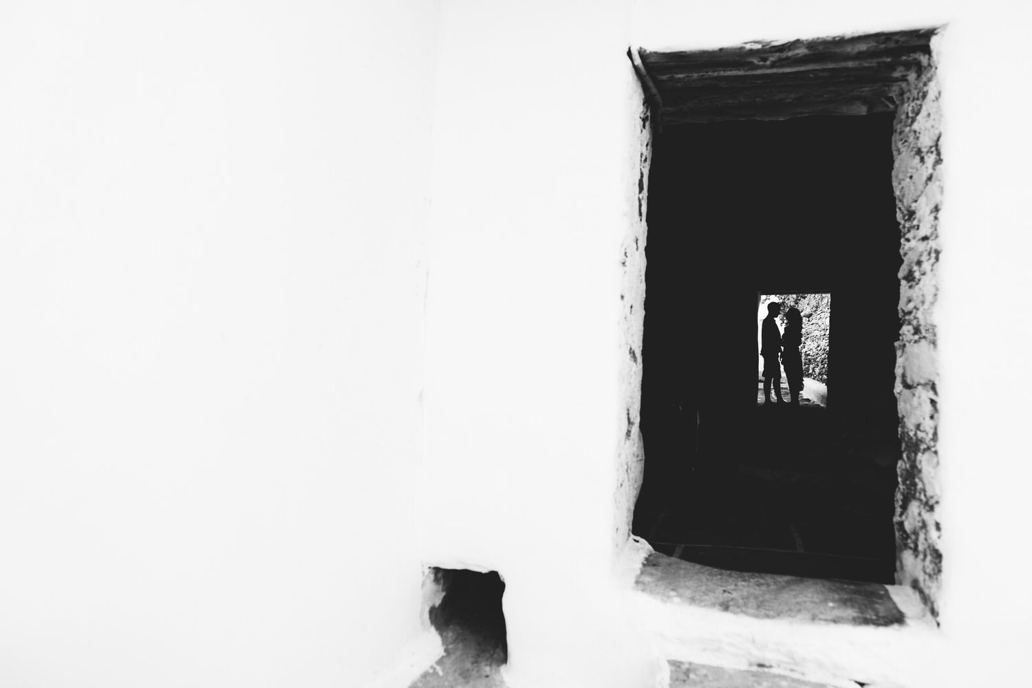 Artistic black and white photograph through stone doorway showing silhouetted figures.