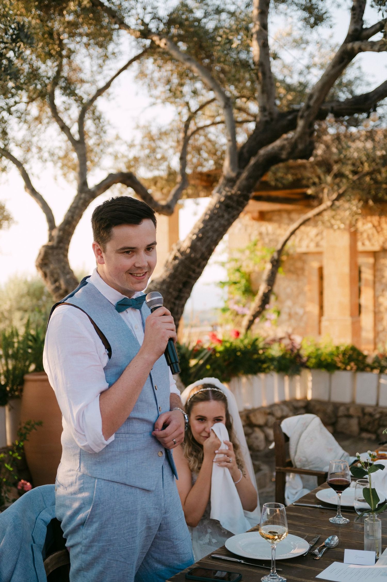 A heartfelt toast takes place during an outdoor wedding reception under a large tree.