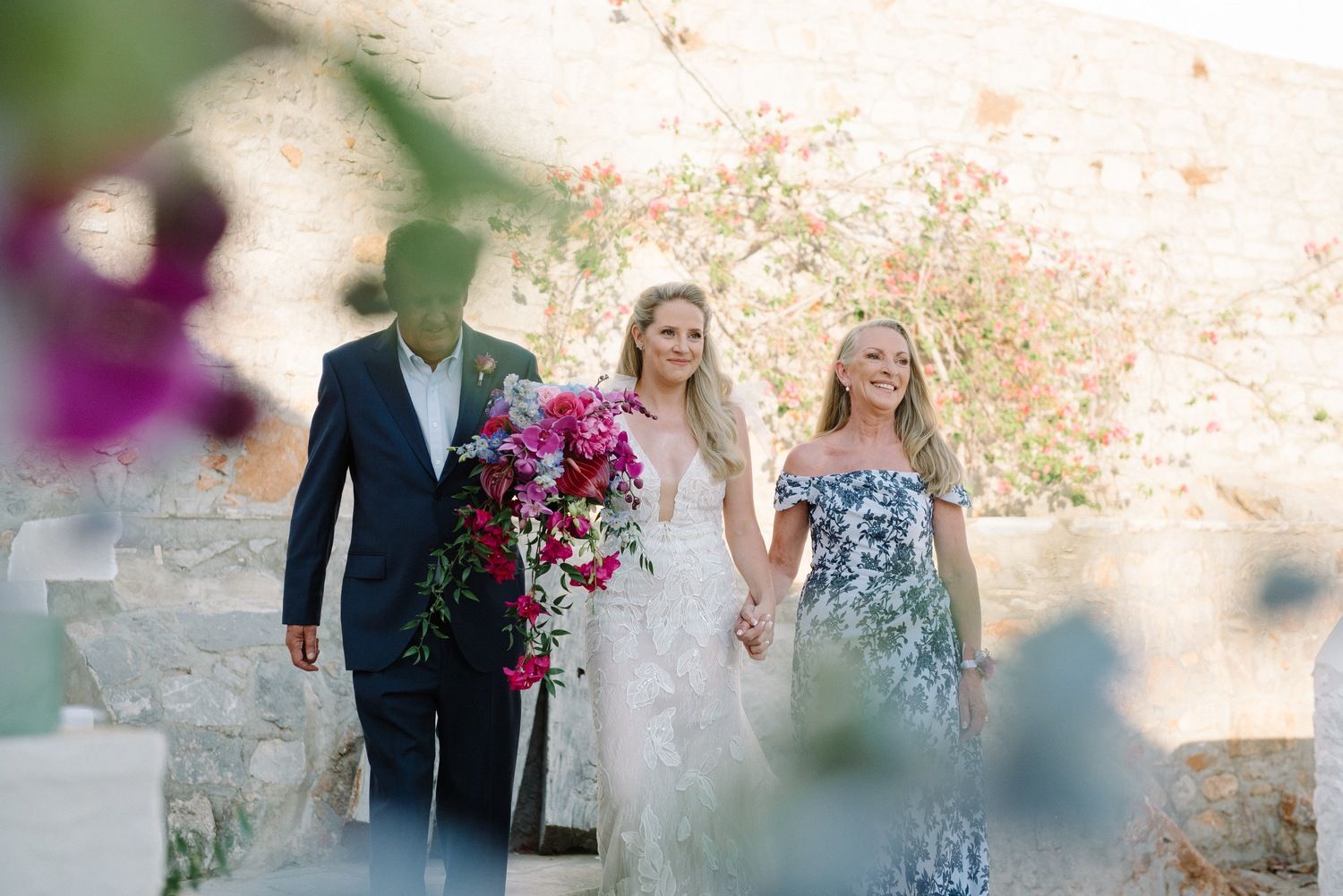Elegant outdoor wedding ceremony with floral arrangements against stone wall backdrop.