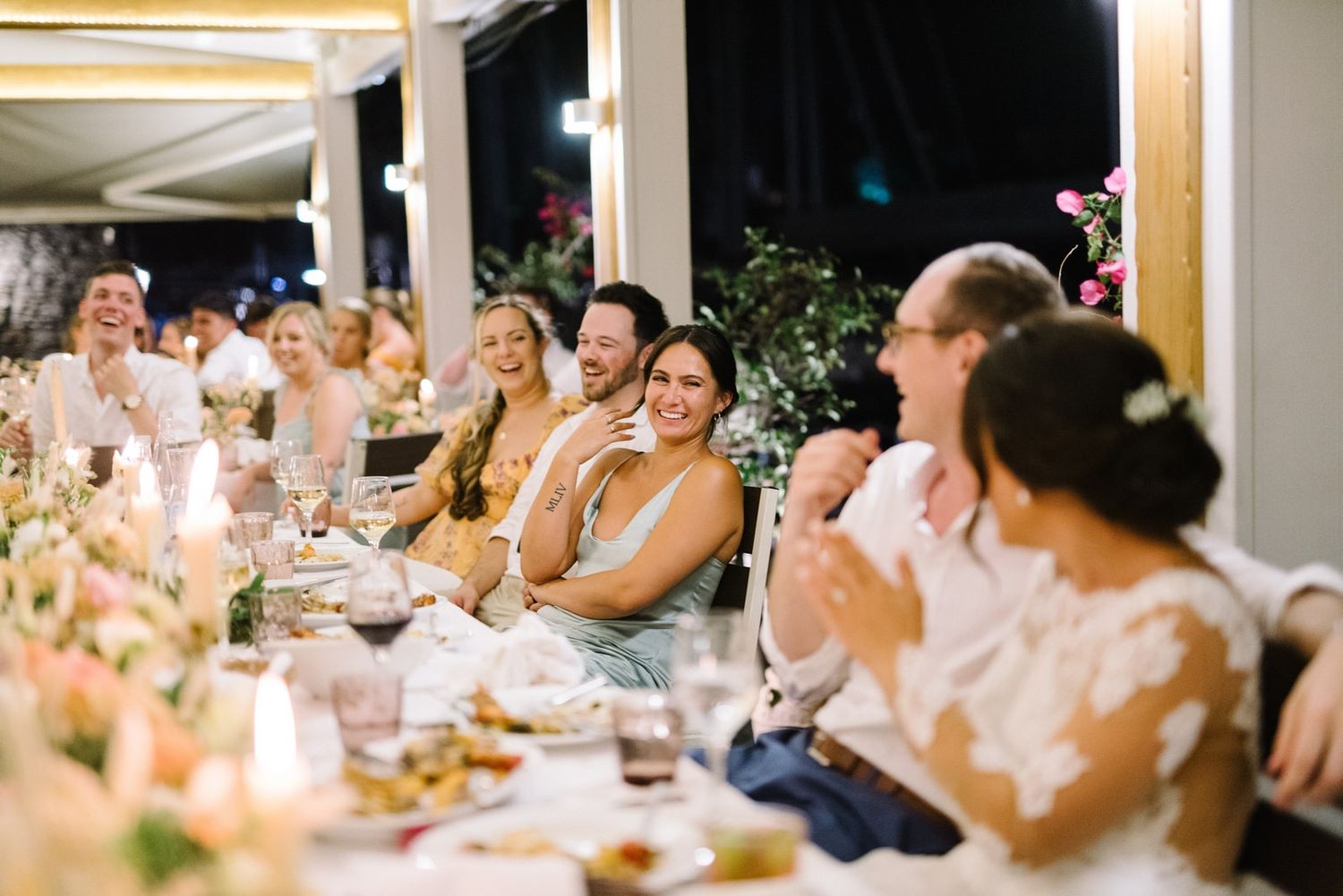 Wedding guests laugh and celebrate during outdoor evening reception.