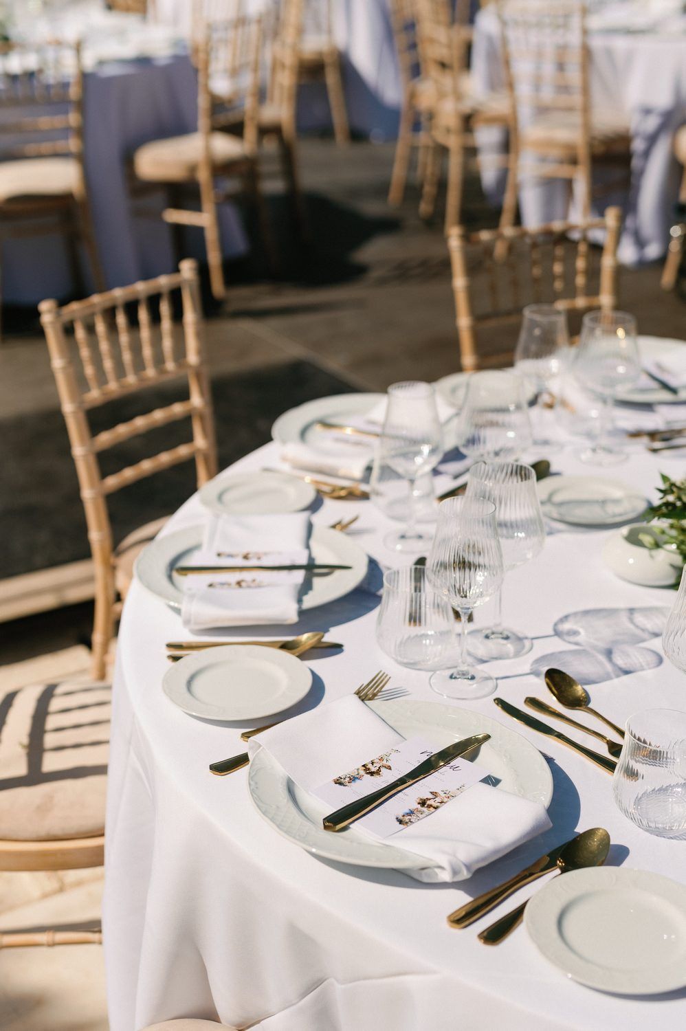 Close-up of formal place setting with gold cutlery on white tablecloth at wedding reception.