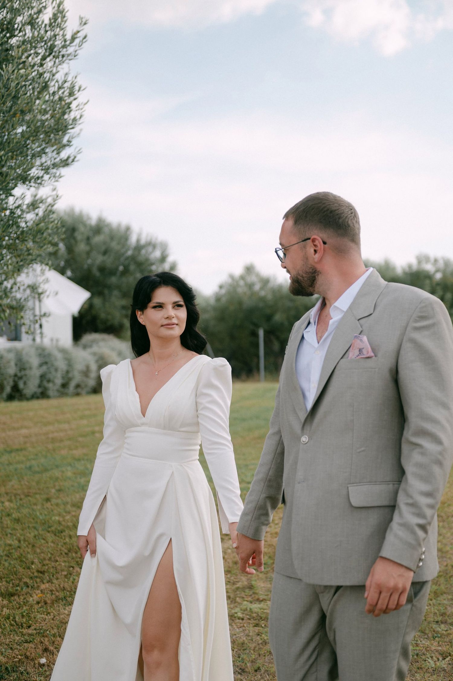 A couple in wedding attire poses together in a grassy field with a romantic, candid atmosphere.
