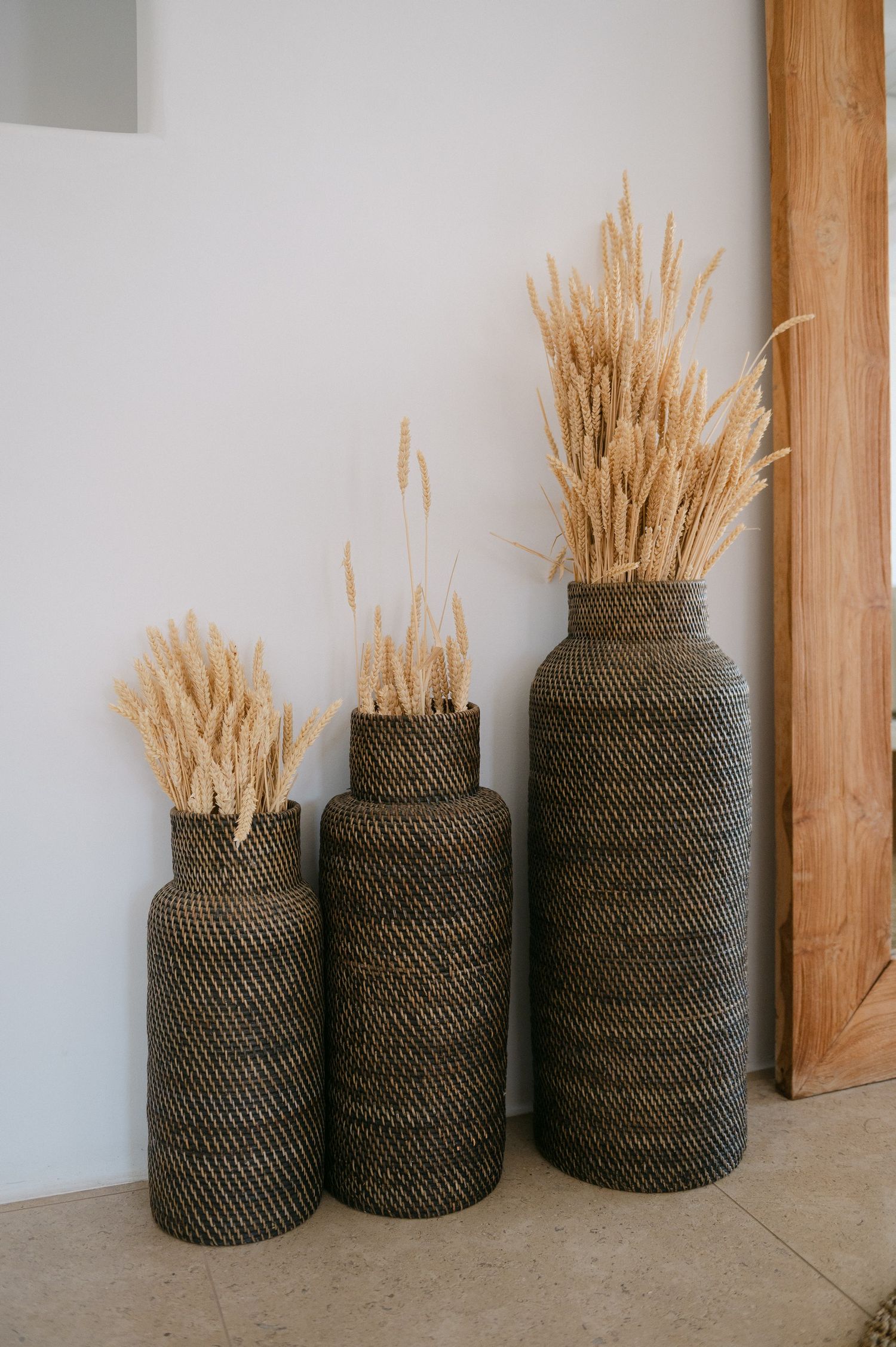 Woven dark rattan baskets filled with dried wheat stalks arranged against a white wall create rustic home decor.