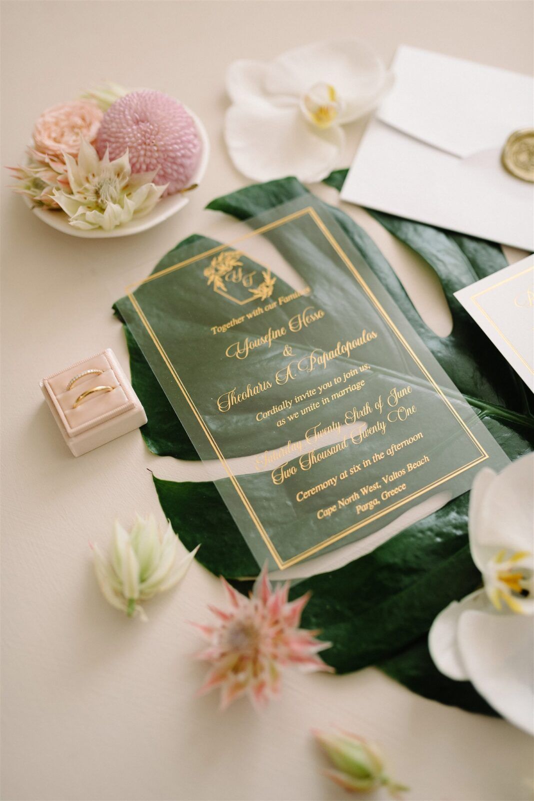 Elegant dark green wedding invitation with gold lettering surrounded by delicate pink and white flowers and foliage.