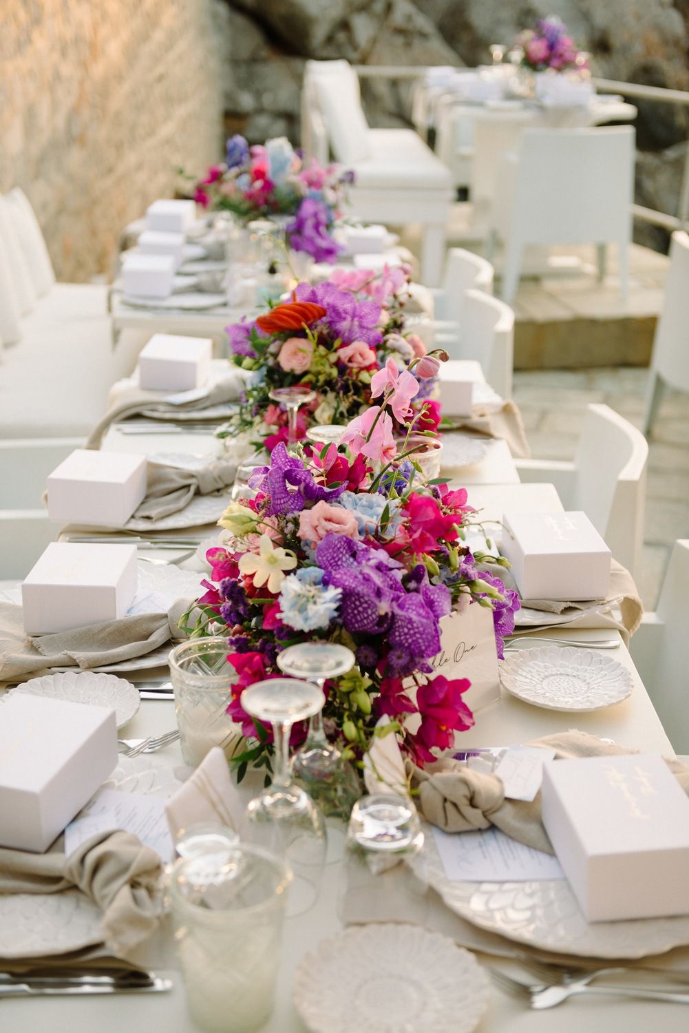 Elegant white table setting with colorful floral runners featuring pink and purple blooms.