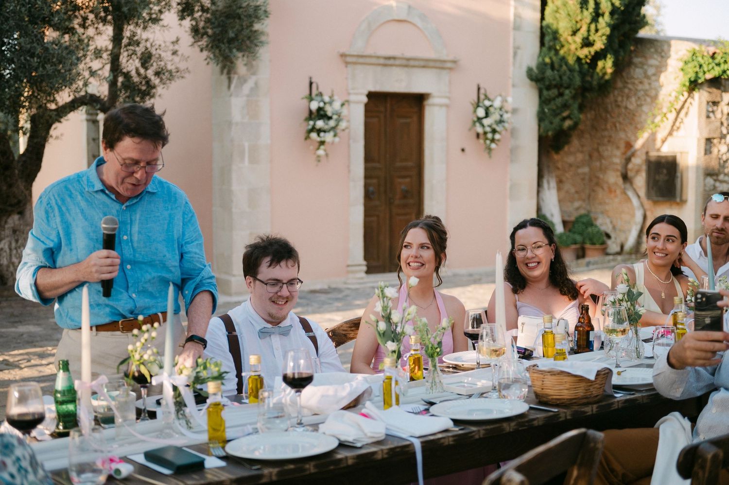 Dinner guests enjoy conversation and wine at a long outdoor table during an evening garden party.