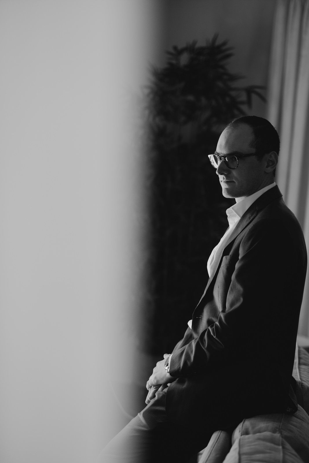 A person in a suit and glasses sits in contemplation against a dark backdrop.