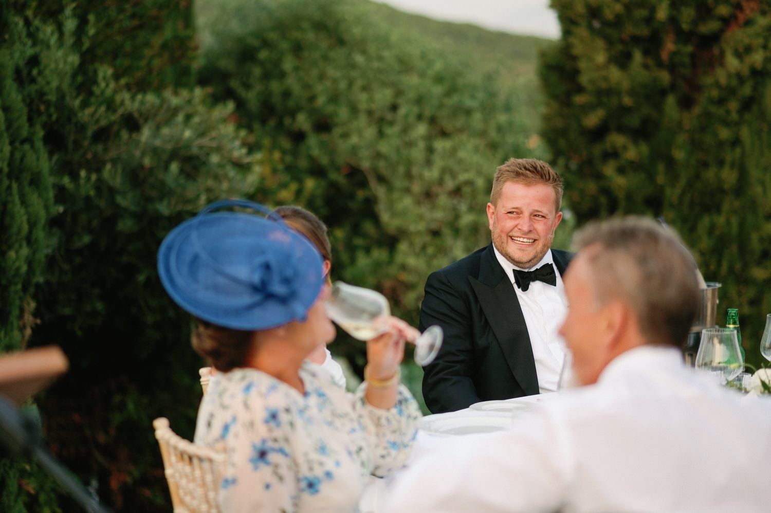 Wedding guests share toasts and laughter during outdoor reception speeches.