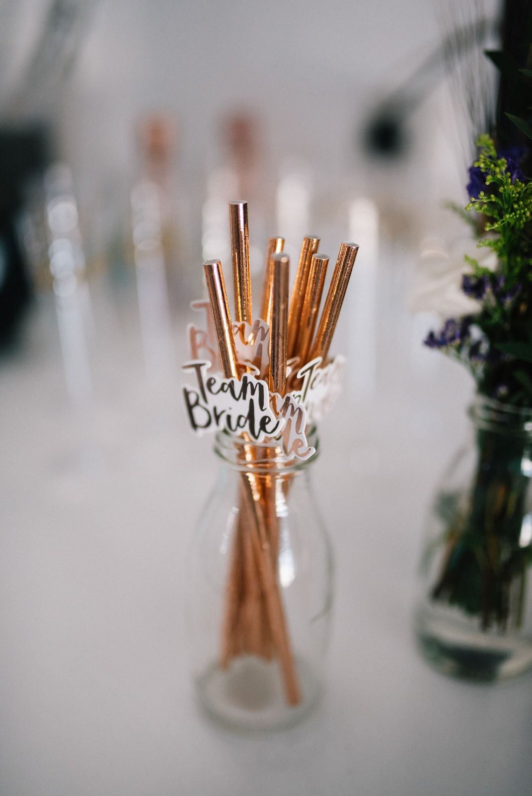 Gold paper straws in a glass jar labeled 'Team Bride' with flowers in background.